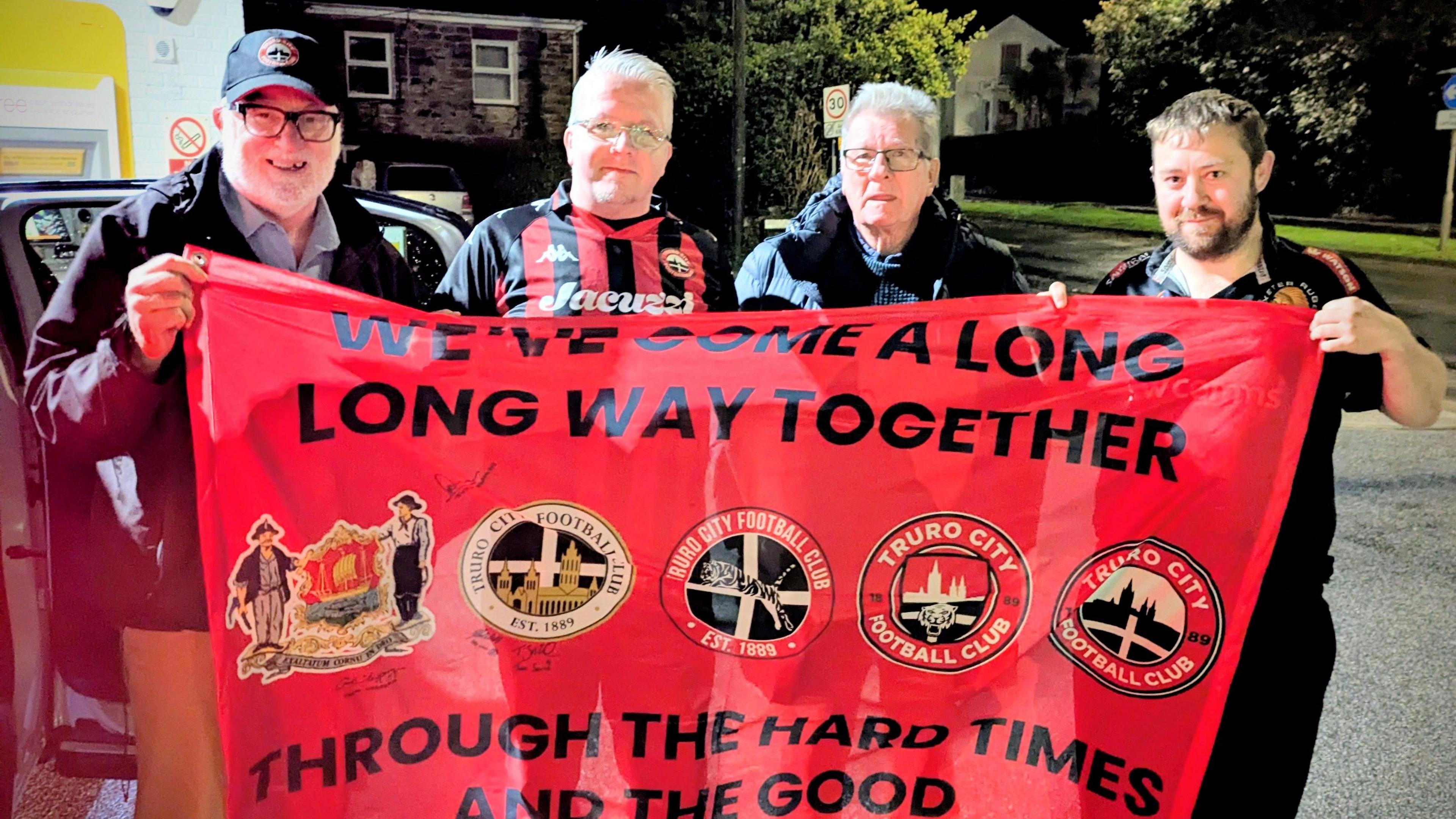 Four Truro fans hold a banner before they set off on the journey to play Gateshead away in the National League