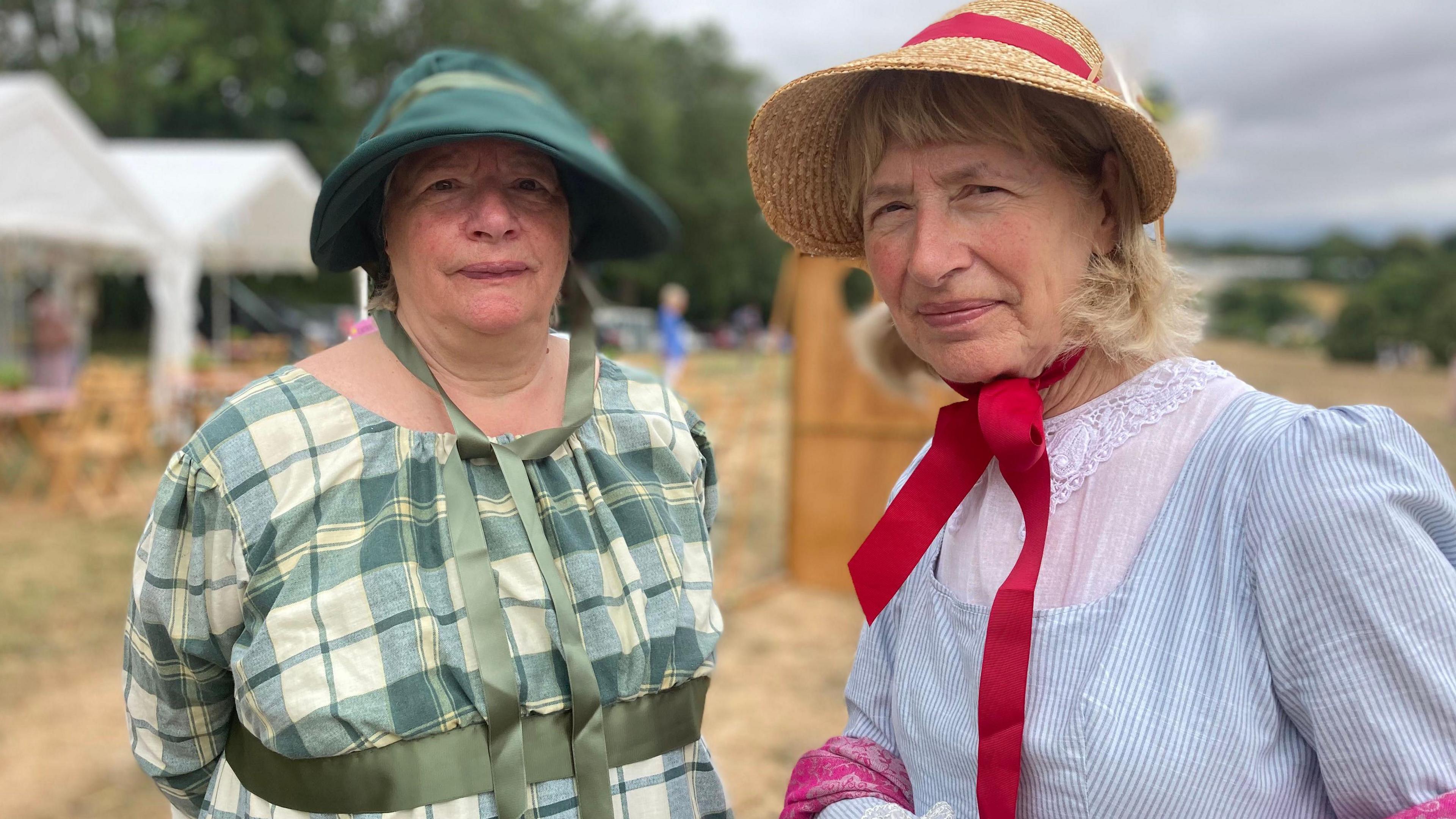 Two women wearing Regency outfits and bonnets with ribbons to tie under their chins.