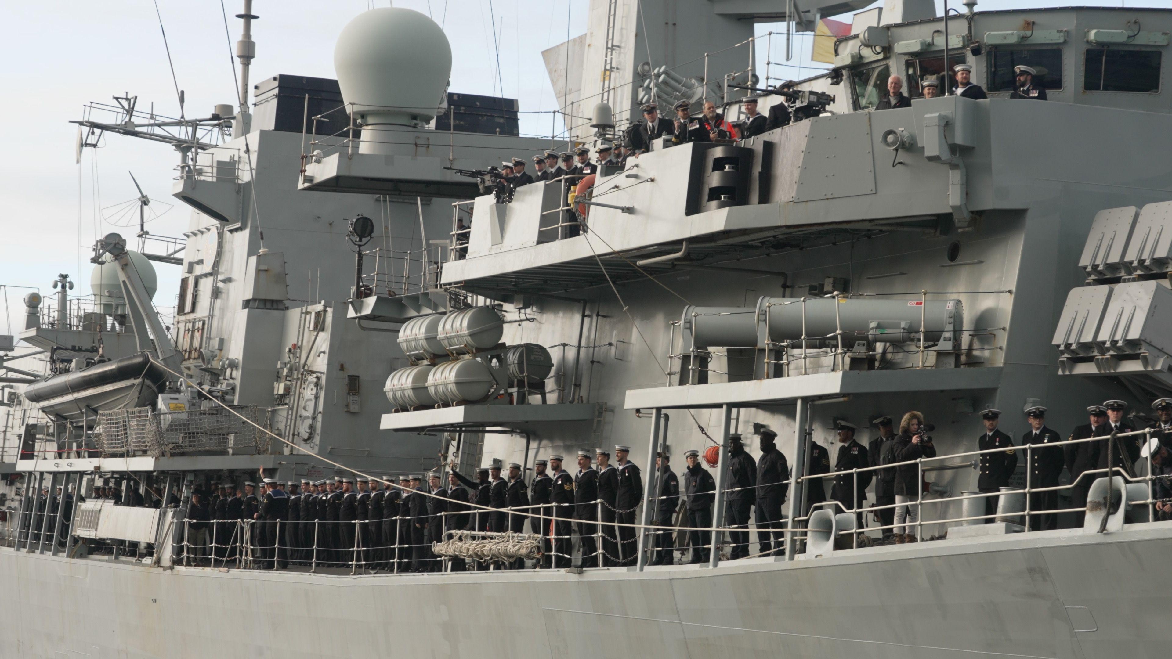 Sailors standing along the side of HMS Richmond in a line. The ship is large and grey, with several levels of decks.