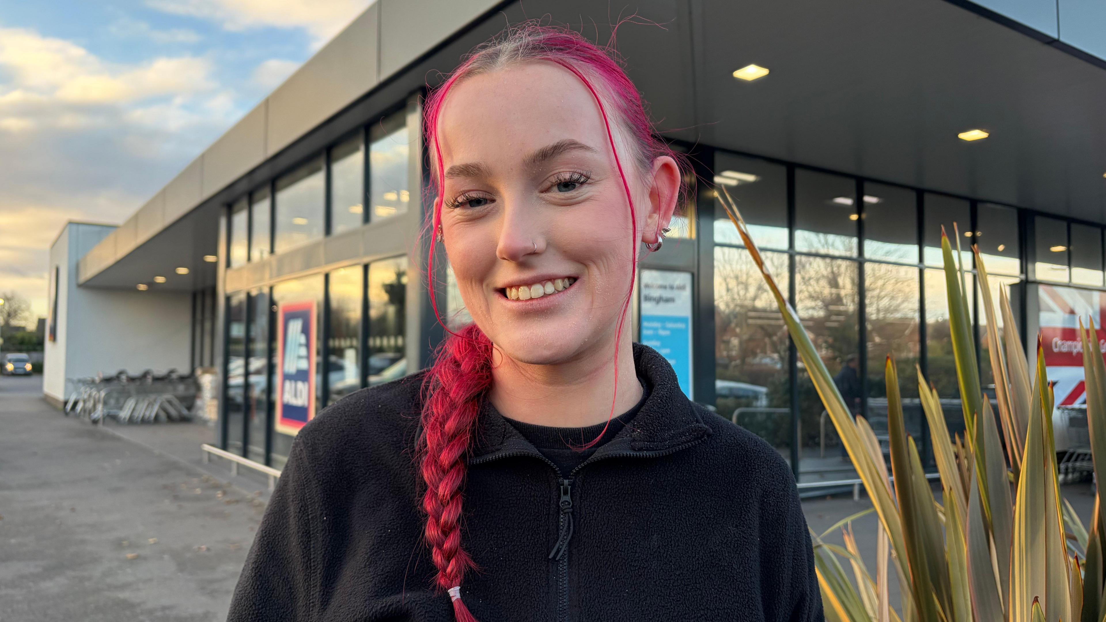Teagan is pictured outside the Aldi store, she has pink hair in a plait.