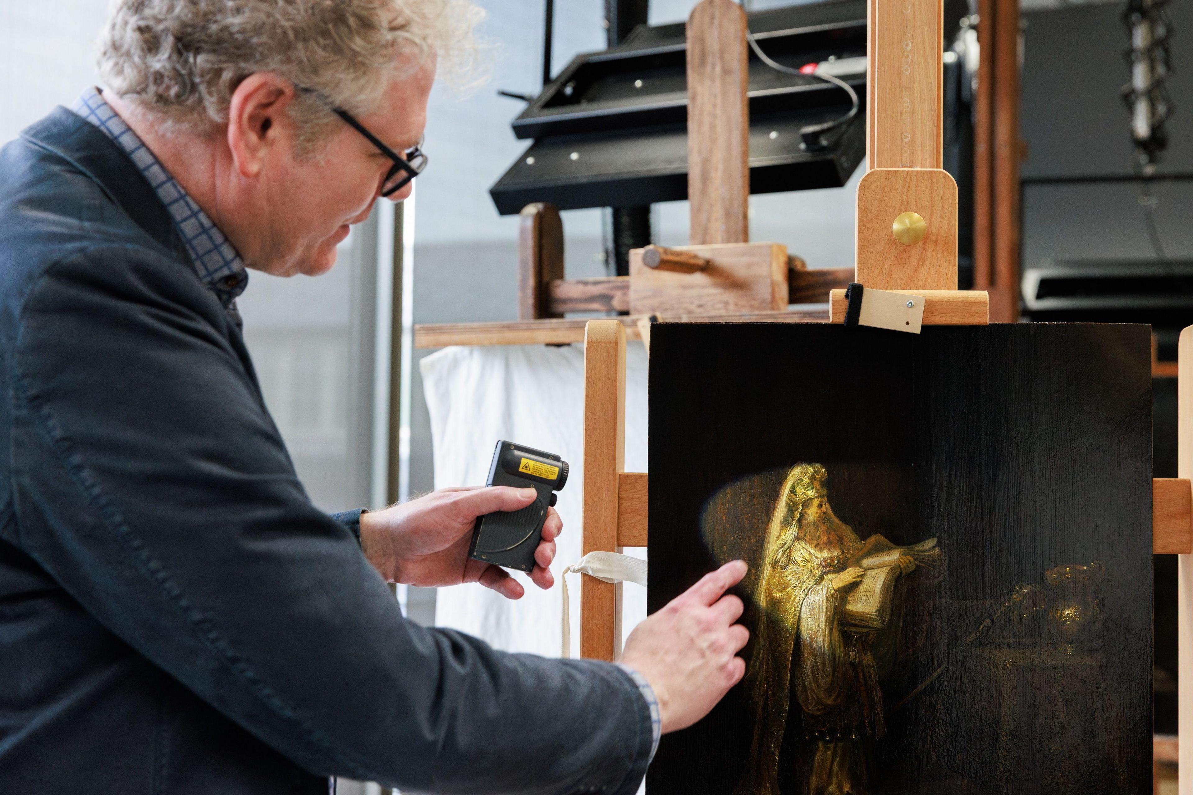 A researcher points at, and points a torch at, the figure of Zacharias from Rembrandt’s Vision of Zacharias in the Temple (1633), which is on an easel