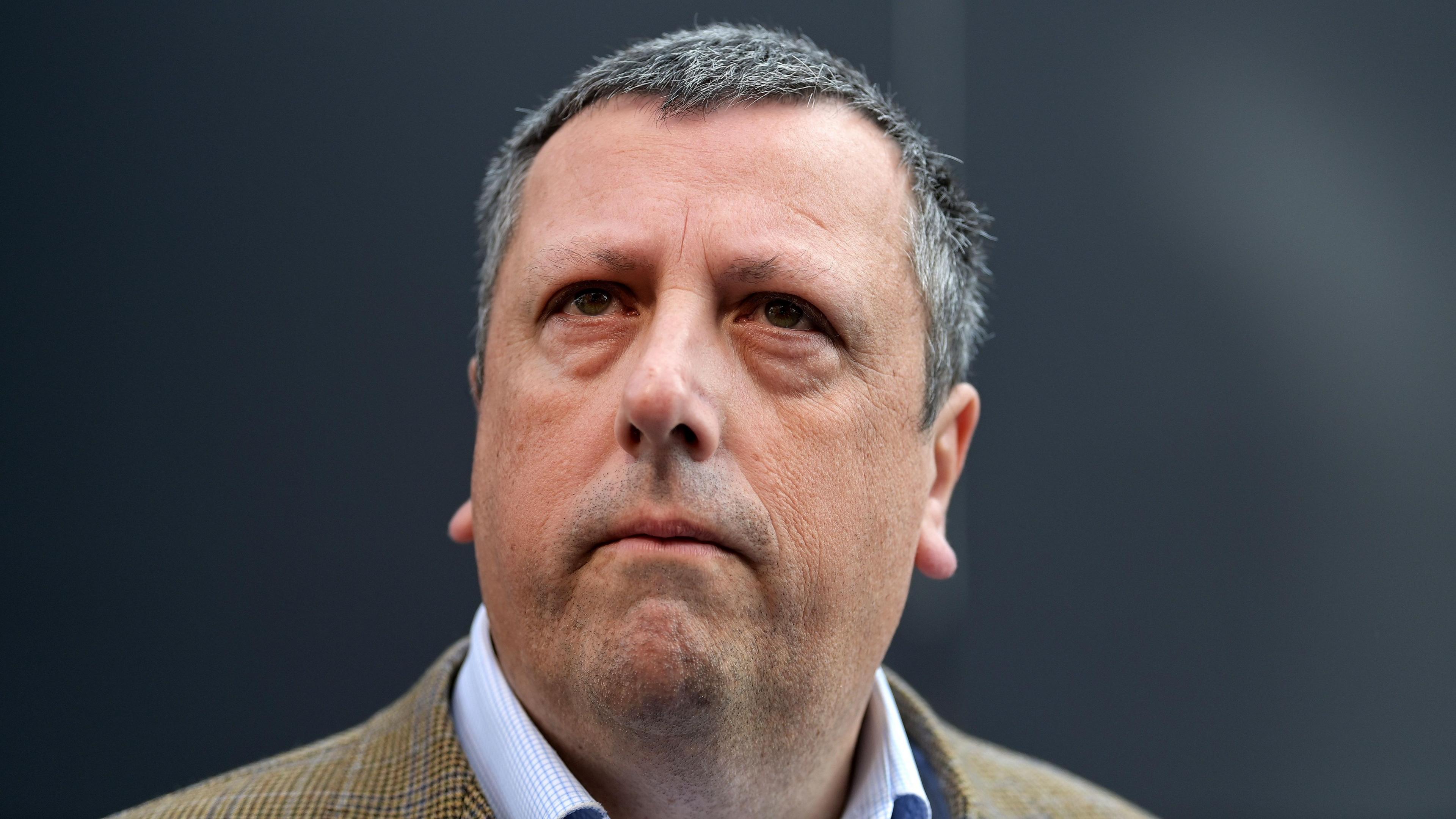 Headshot of David Campebll looking above the camera lens. He is wearing a tweed jacket and a light blue shirt