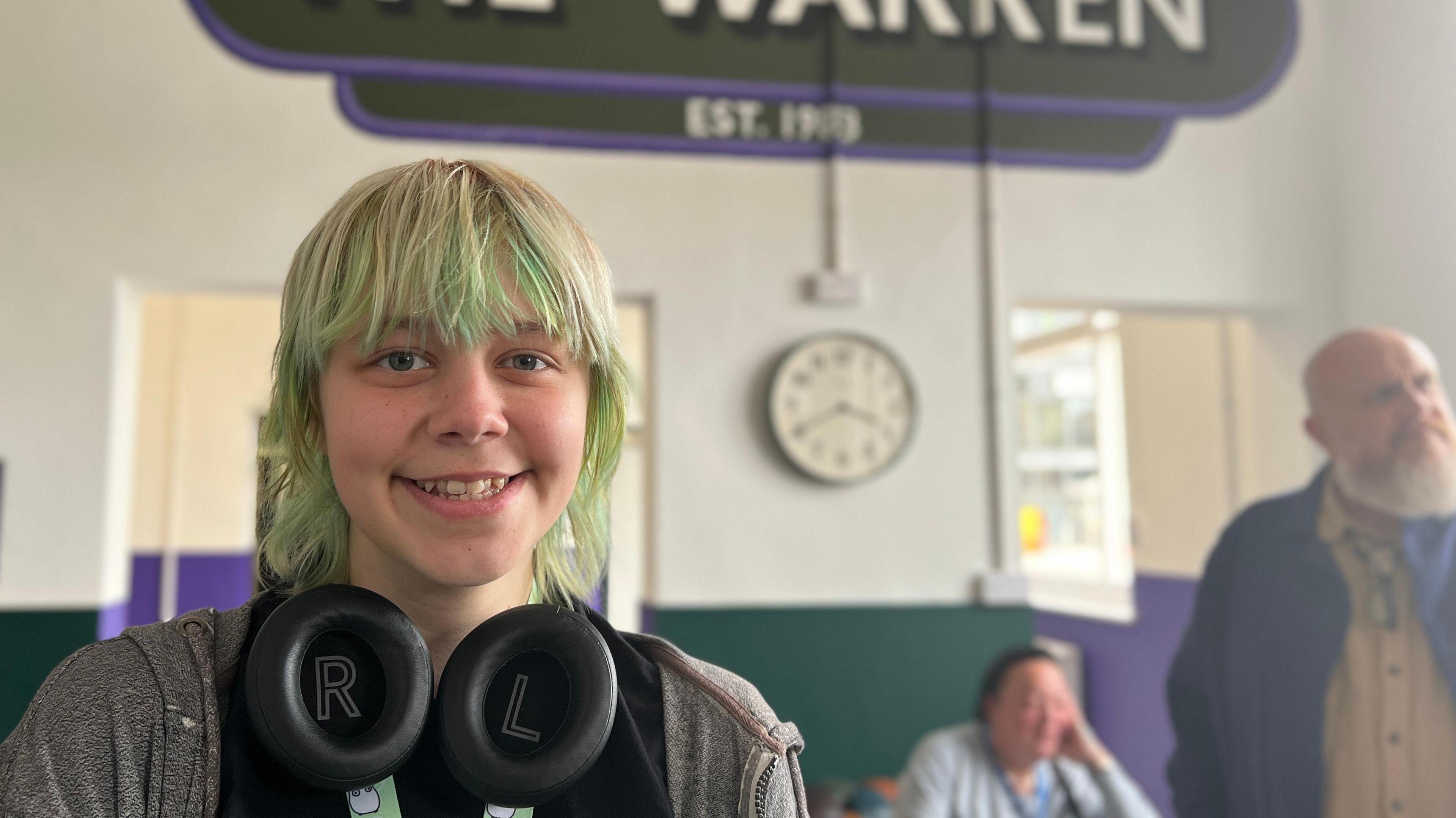 Cricket, who identifies as they/them, has green hair and has headphones around the neck.