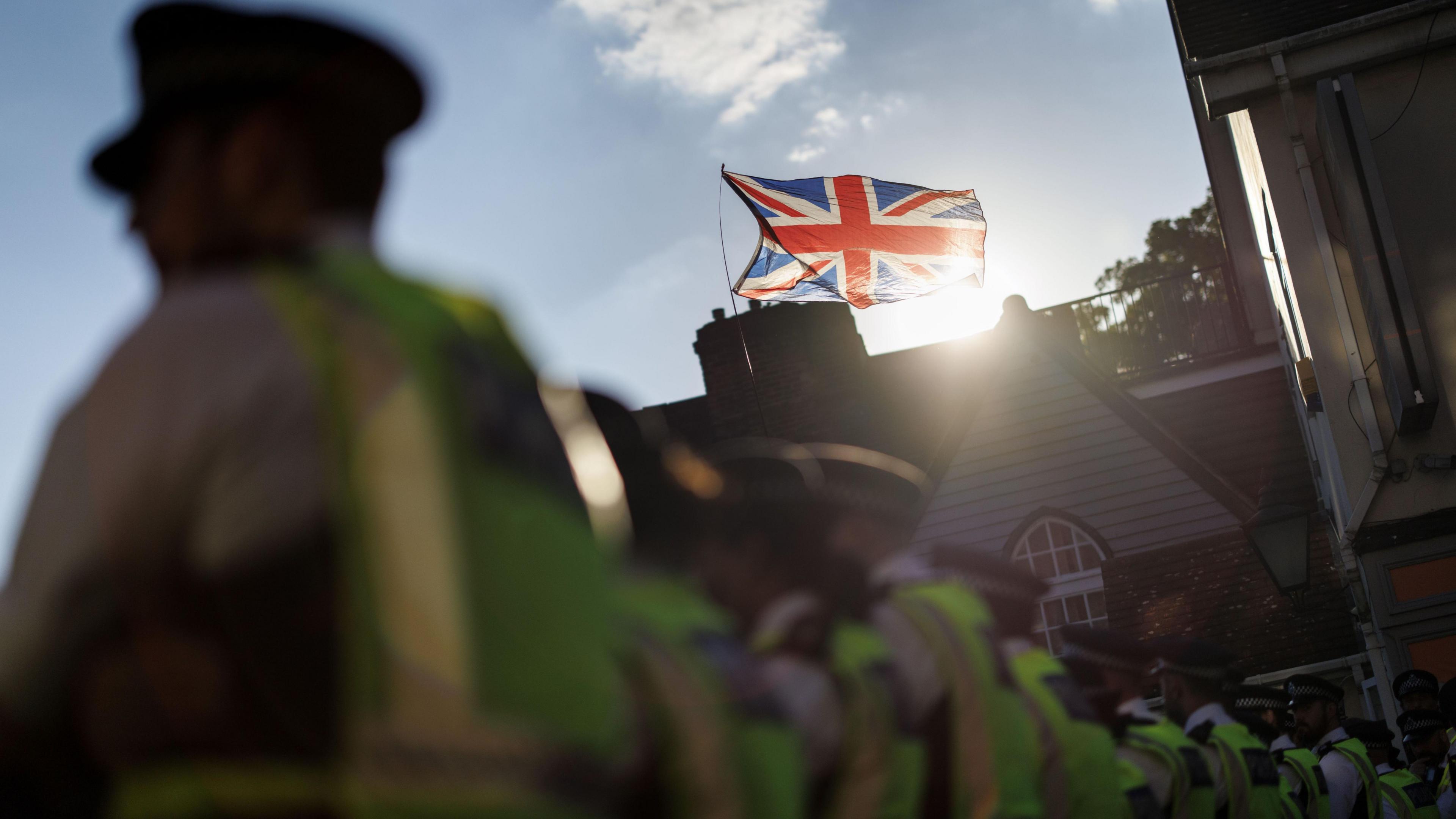 A line of police officers in high-vis uniforms stand in front of a building flying a union flag