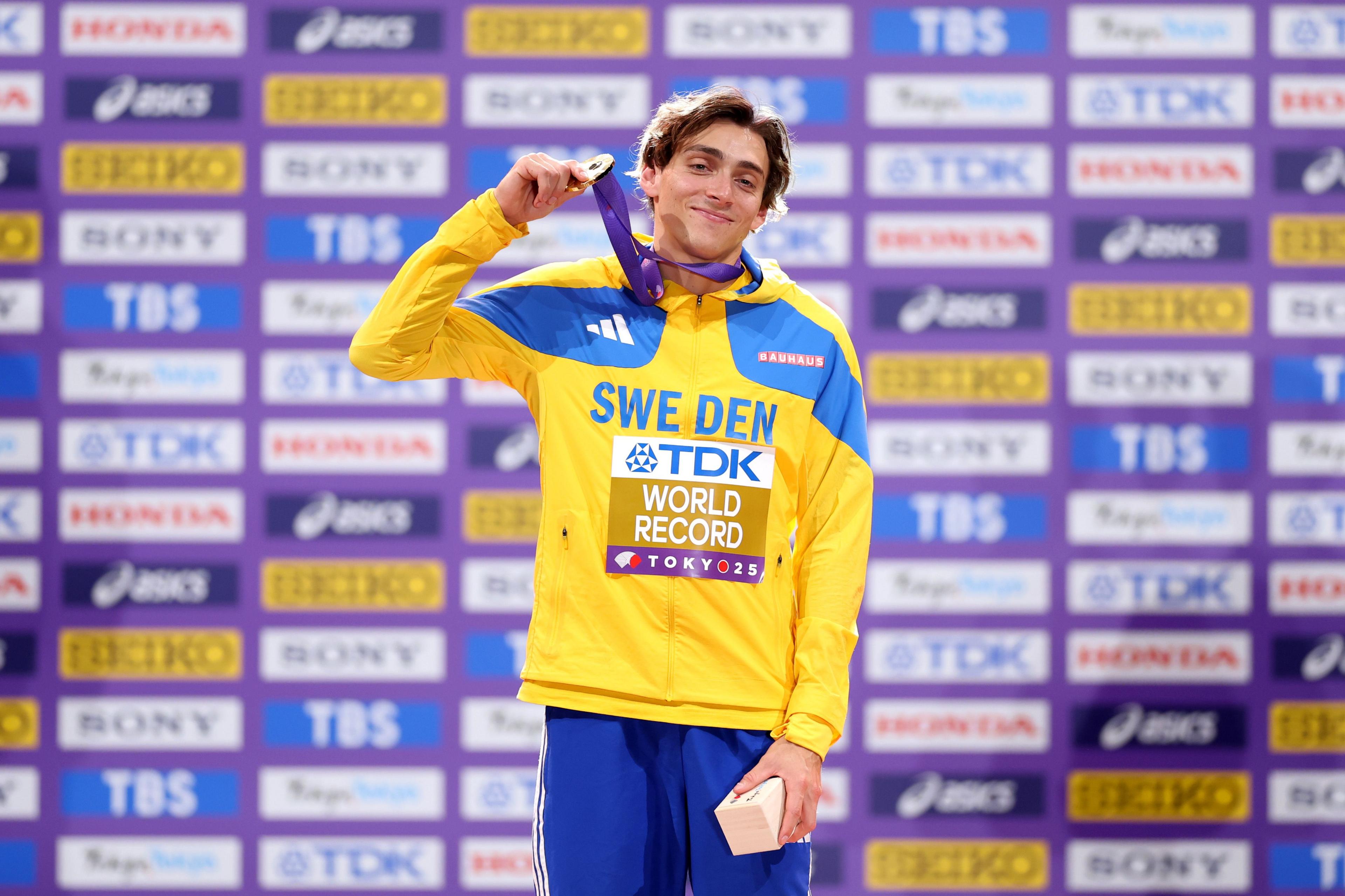 Armand Duplantis poses with his men's pole vault gold medal and a 'world record' sign on his jacket
