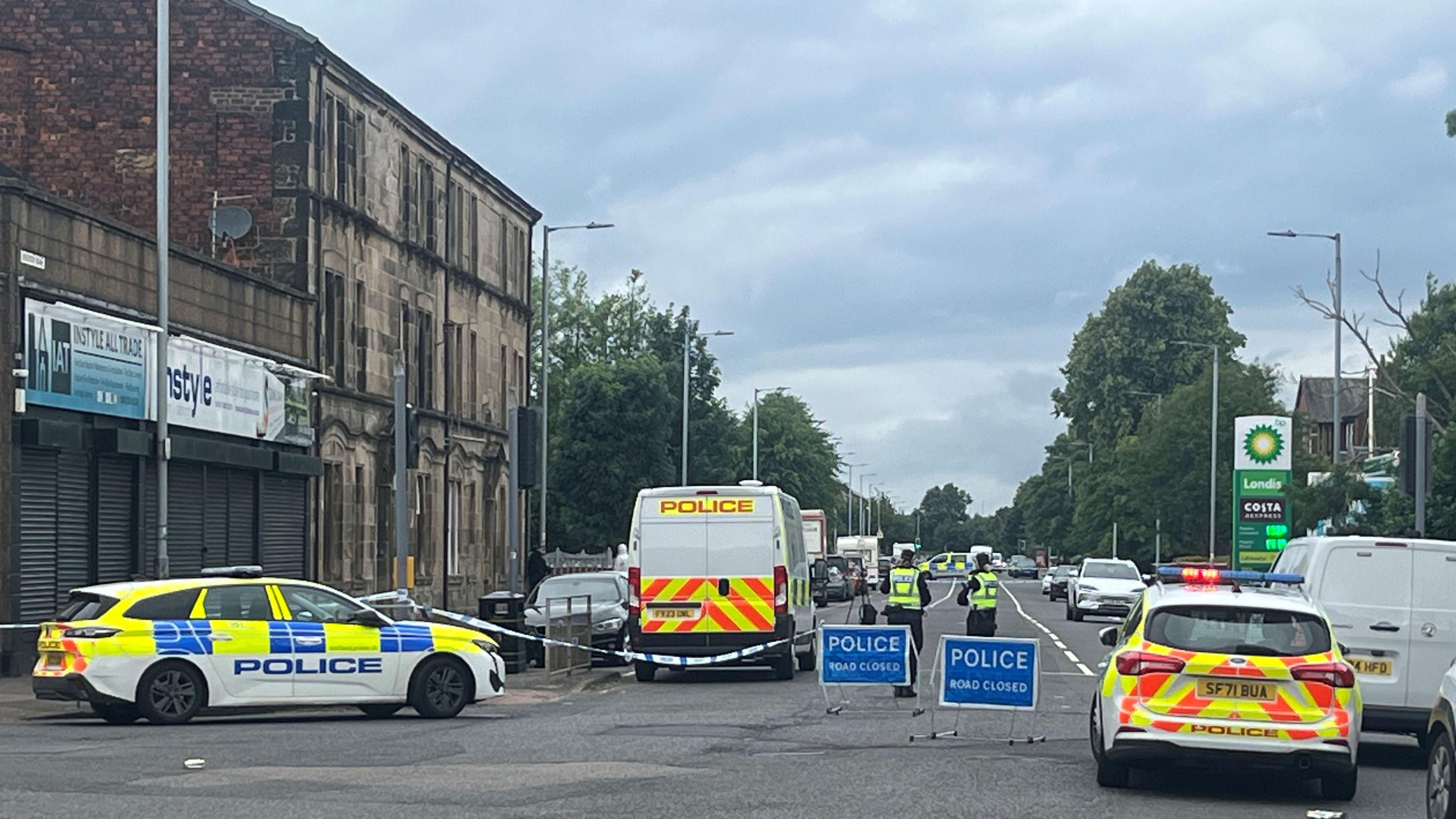 A police scene in Paisley - there are vans, police cars and ROAD CLOSED signs across the area, and officers in high vis vests standing at the scene