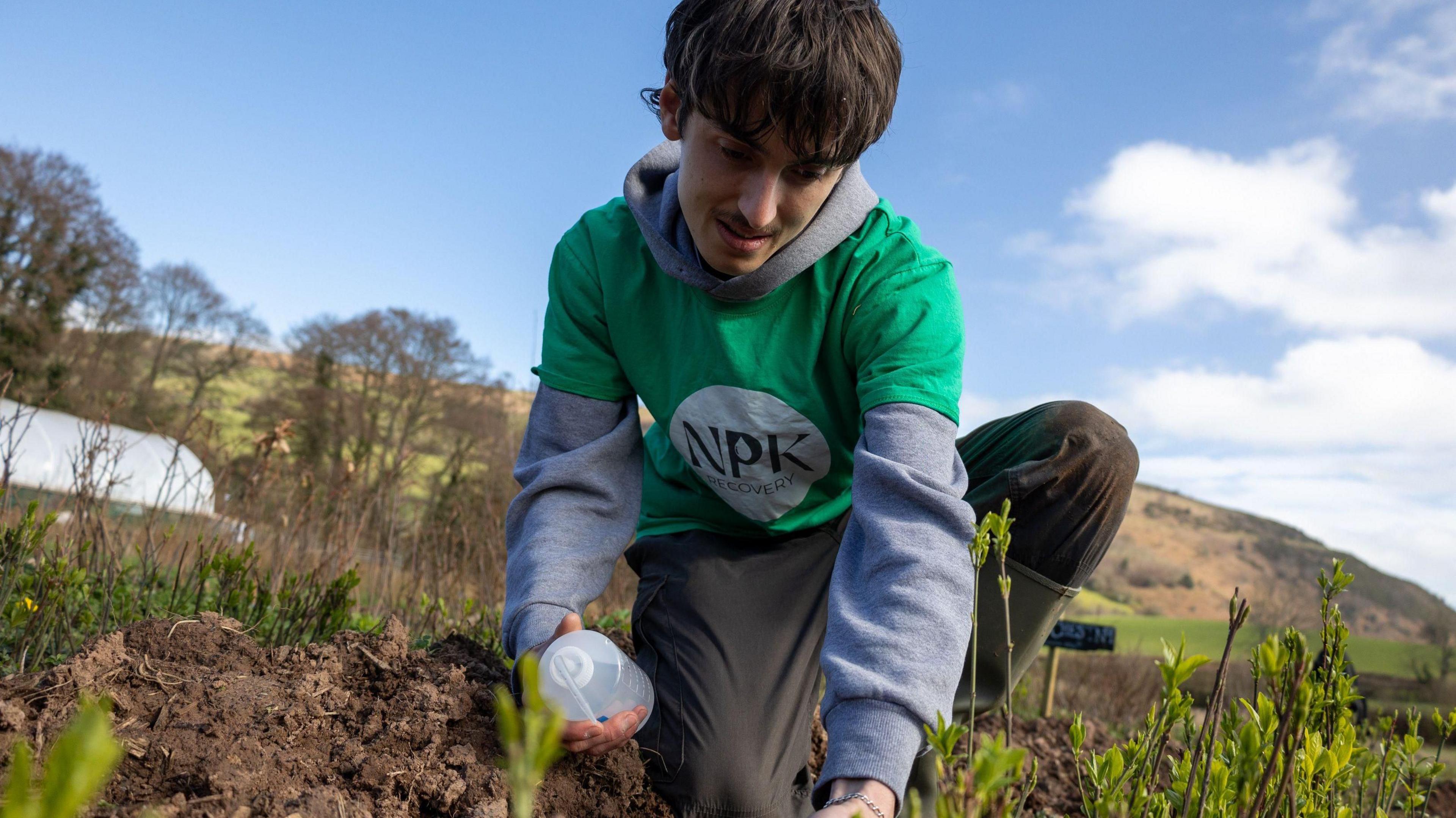 Aelod o dim NPK Recovery yn profi'r pridd yn y feithrinfa goed ger y Fenni