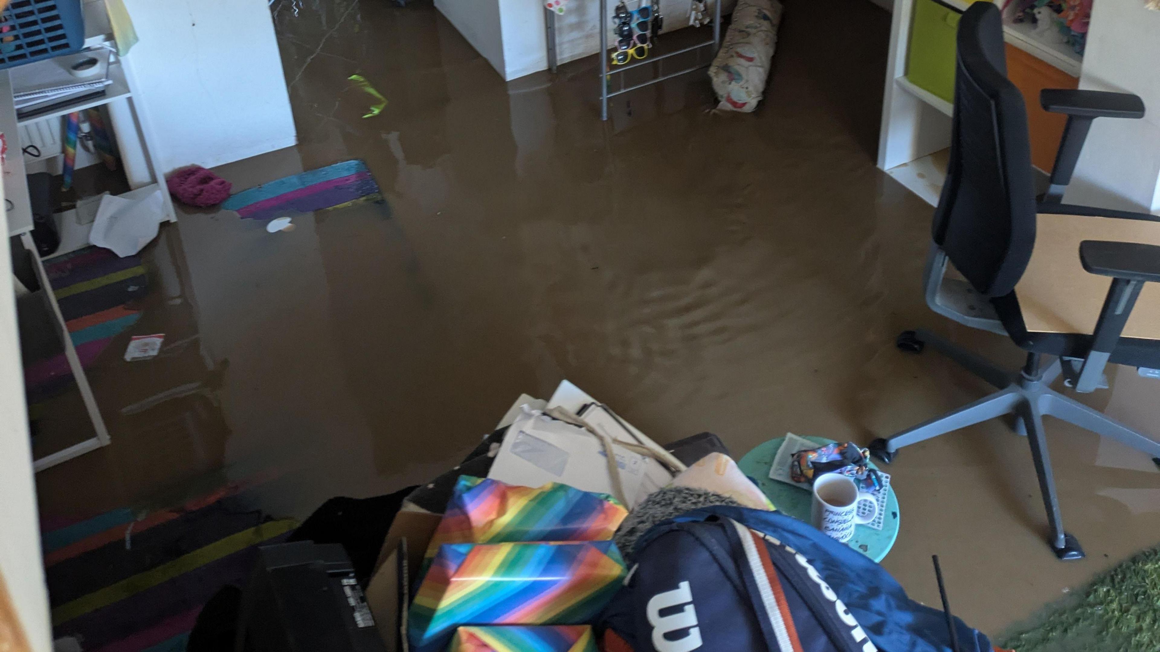 A room in a house in Ilminster in Somerset that is submerged in brown flood water. Various belongings have been piled into a box to be safe from the water and furniture can be seen standing in it