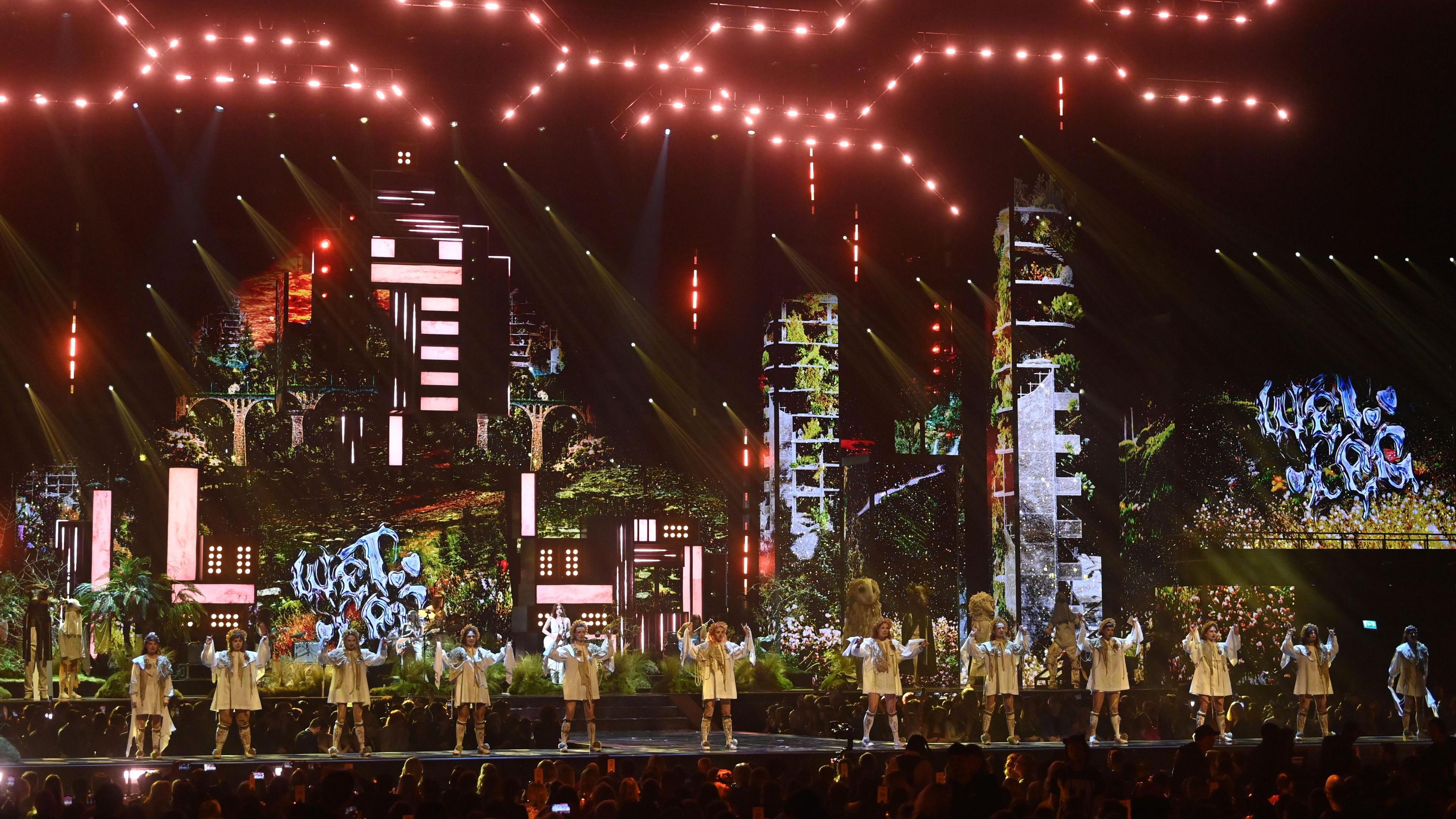 Brit Awards stage with Boss Morris members standing in a line in front of Wet Leg. Behind them both is an urban-looking tall set.