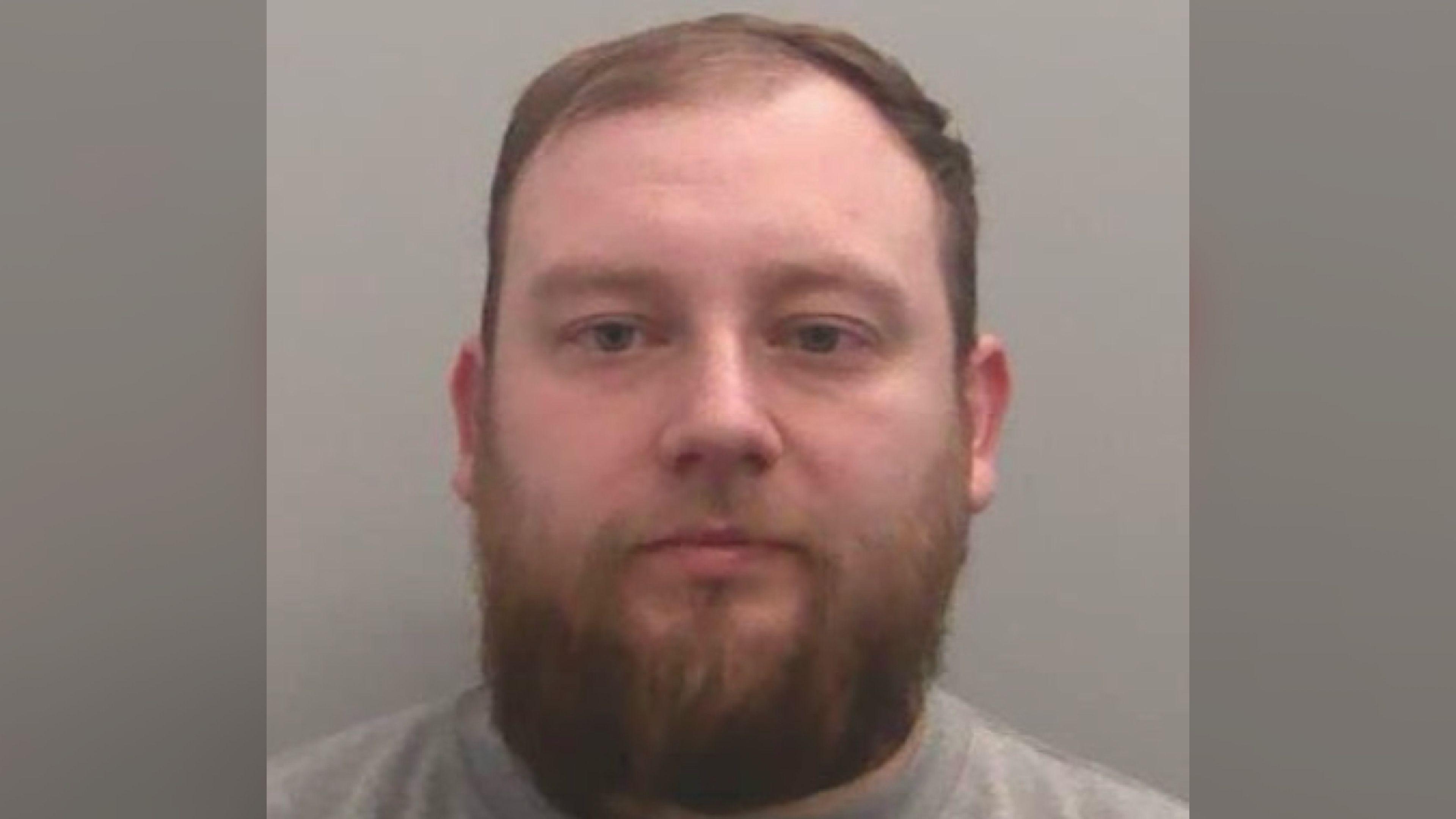 Sam Elphick's mug shot. A man with short brown hair a thick, dark beard.