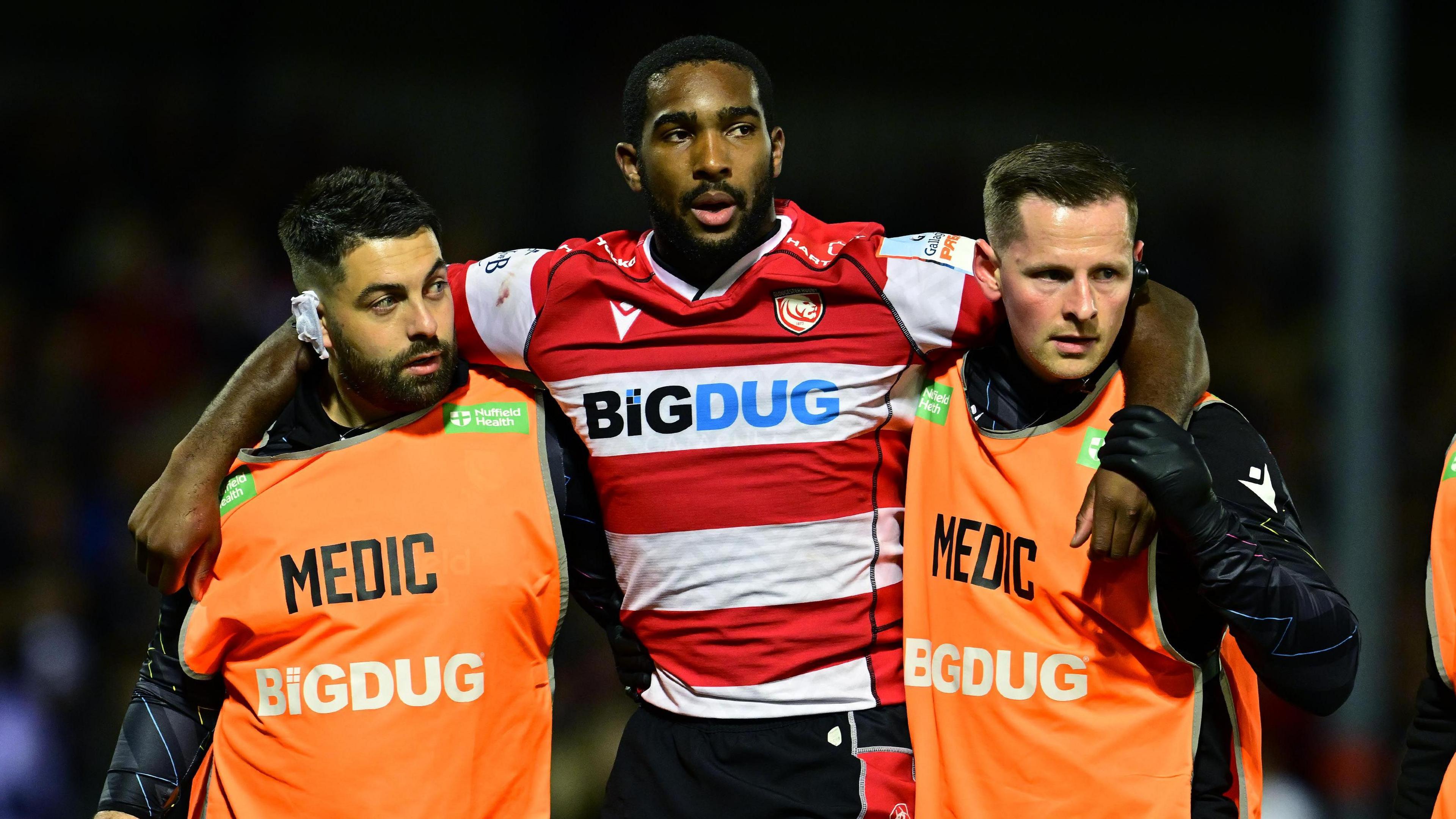 Josiah Edwards-Giraud holds his arms around two medics as he is helped off the field