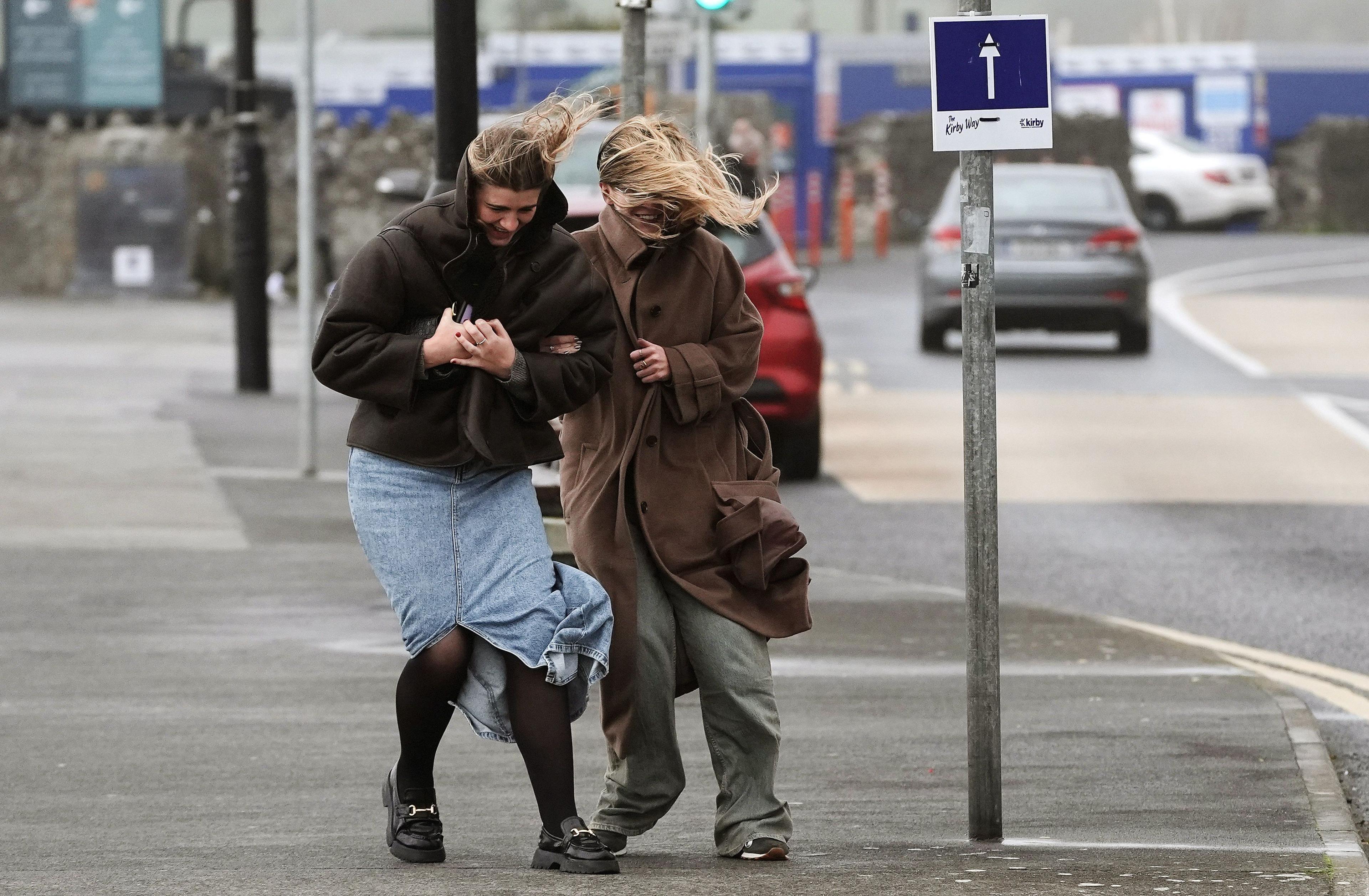 Two women walk along a pavement in strong winds