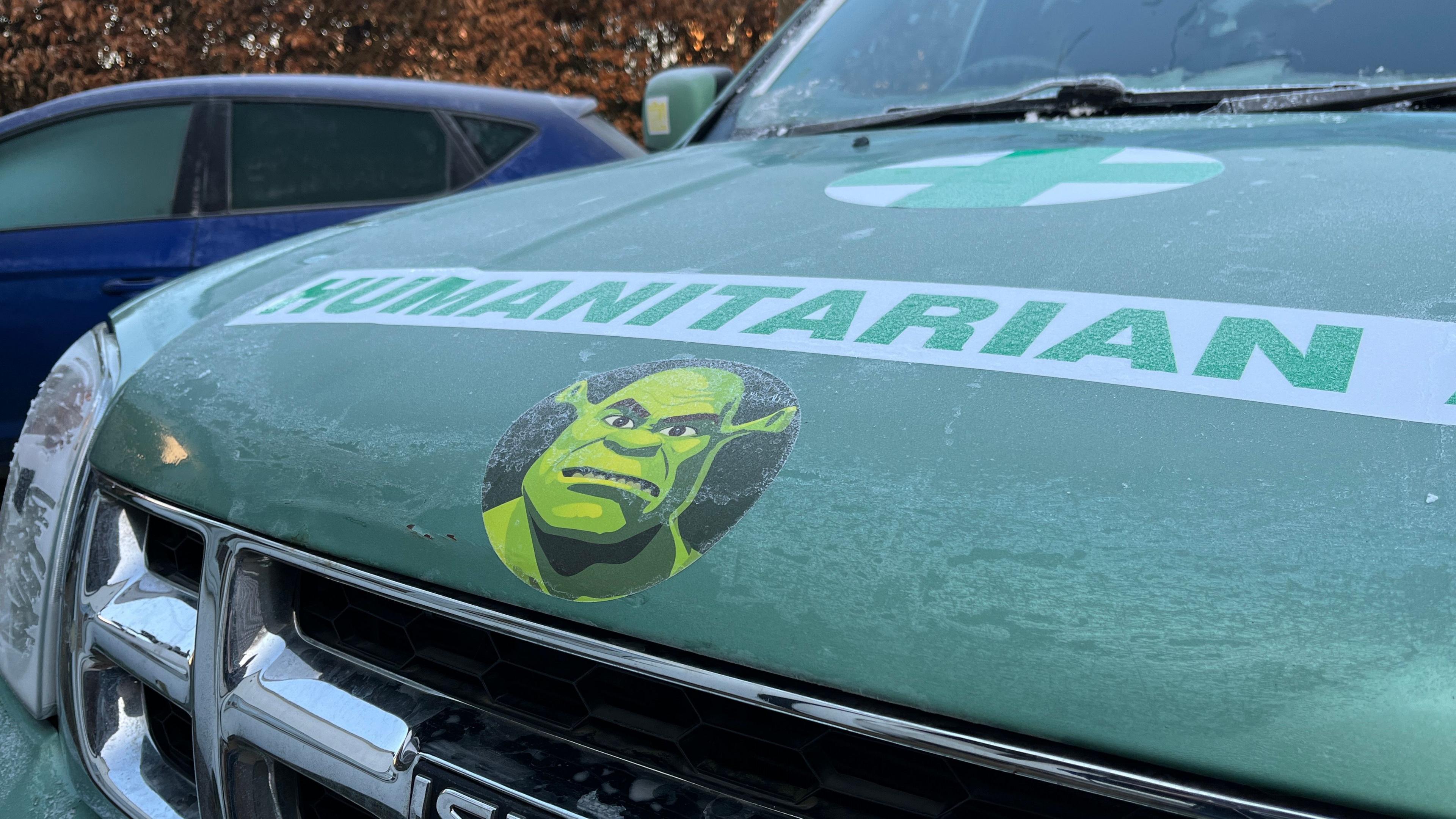 The front of the 4x4 has a circle sticker of Shrek - a green ogre - on the front. Above it are the words humanitarian aid and a medical sticker.