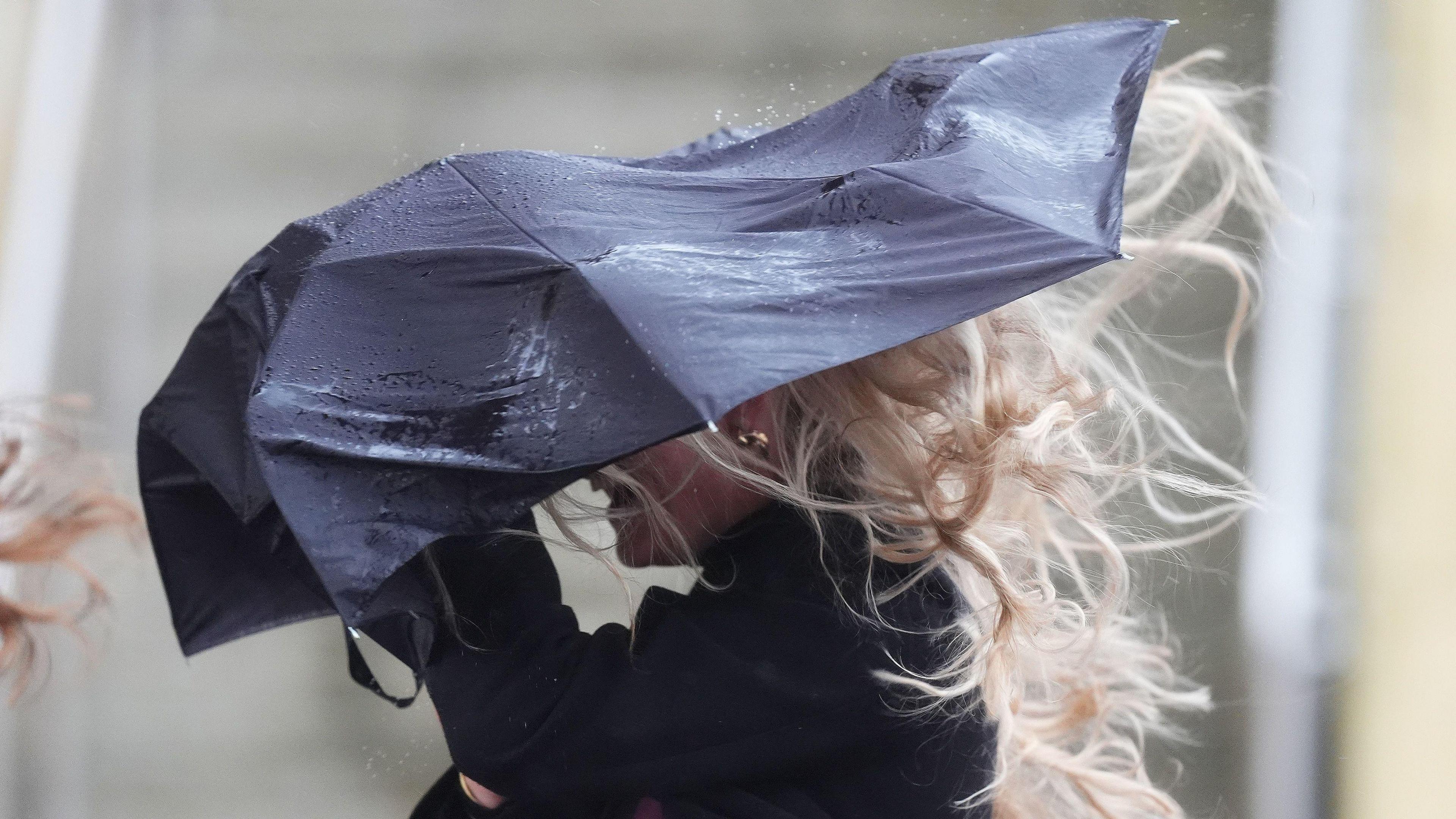 A woman walking with her umbrella in heavy wind and rain.