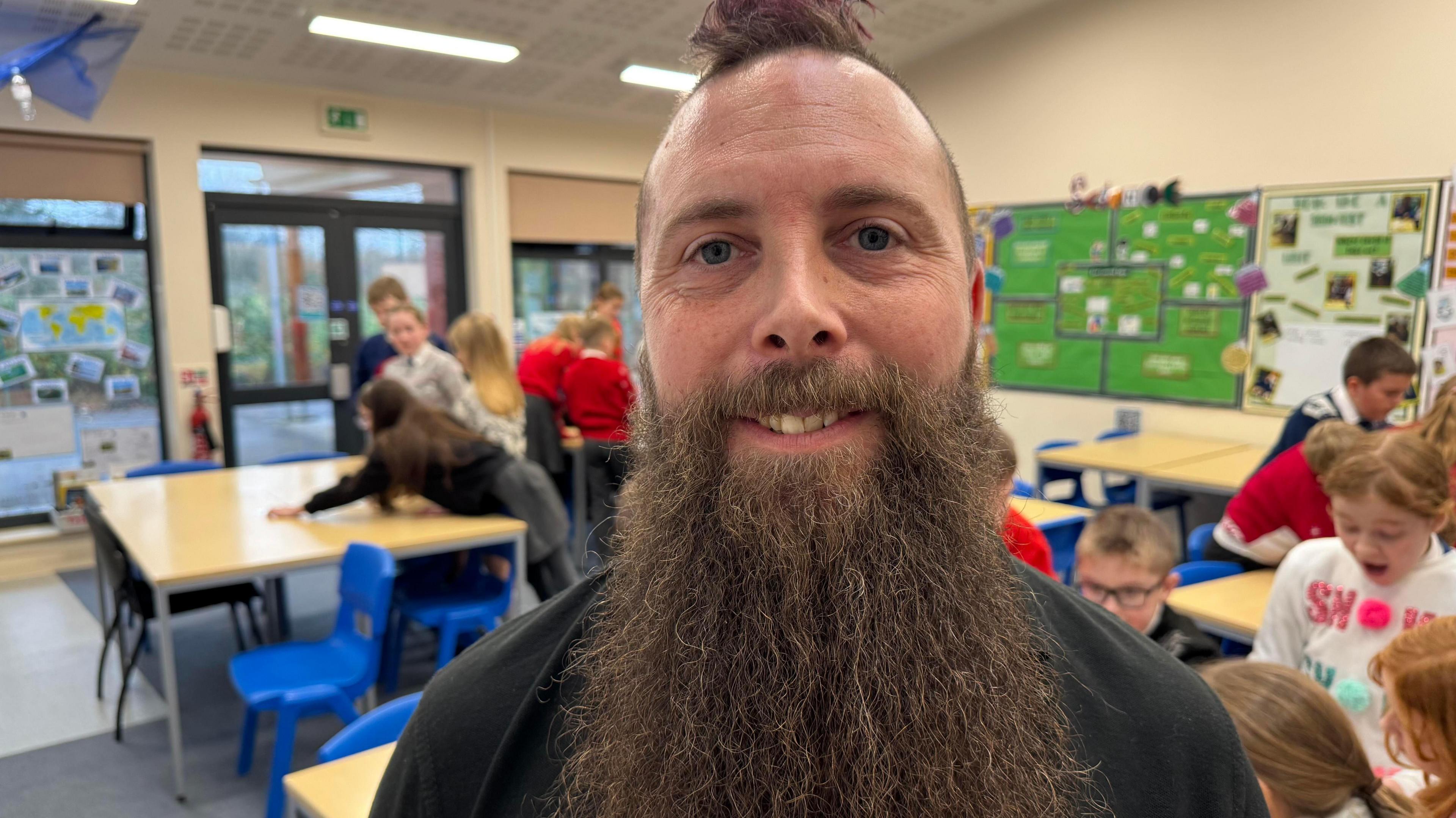 A man smiling at the camera with a very long, brown beard