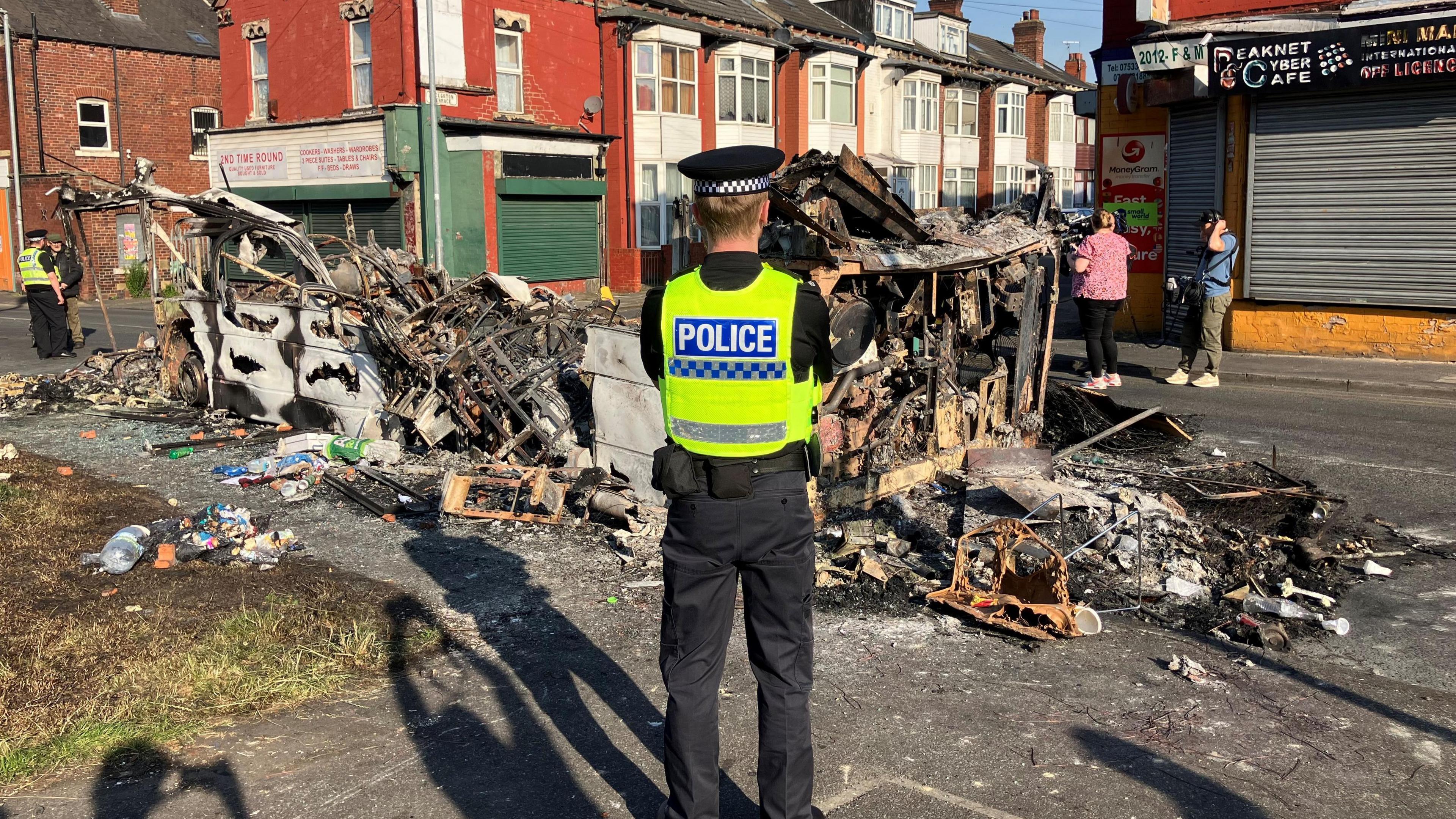 A police officer stands guard over a burnt-out bus.