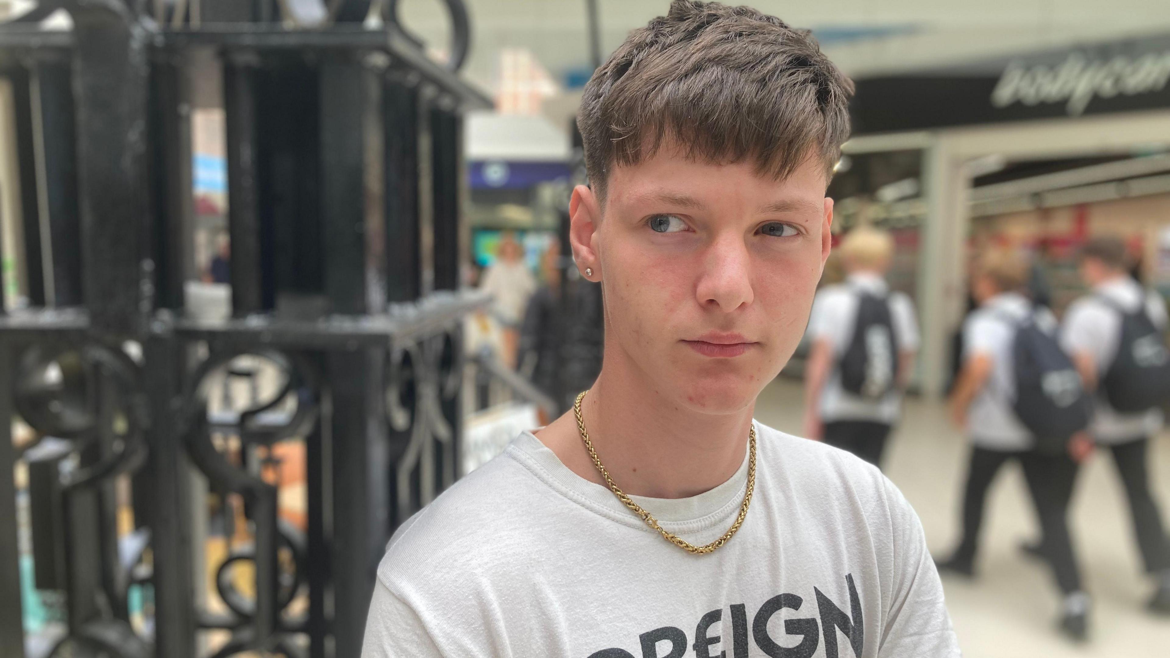 Kowann O'Neill. He has short brunette hair and is wearing a gold chain and a stud earring.