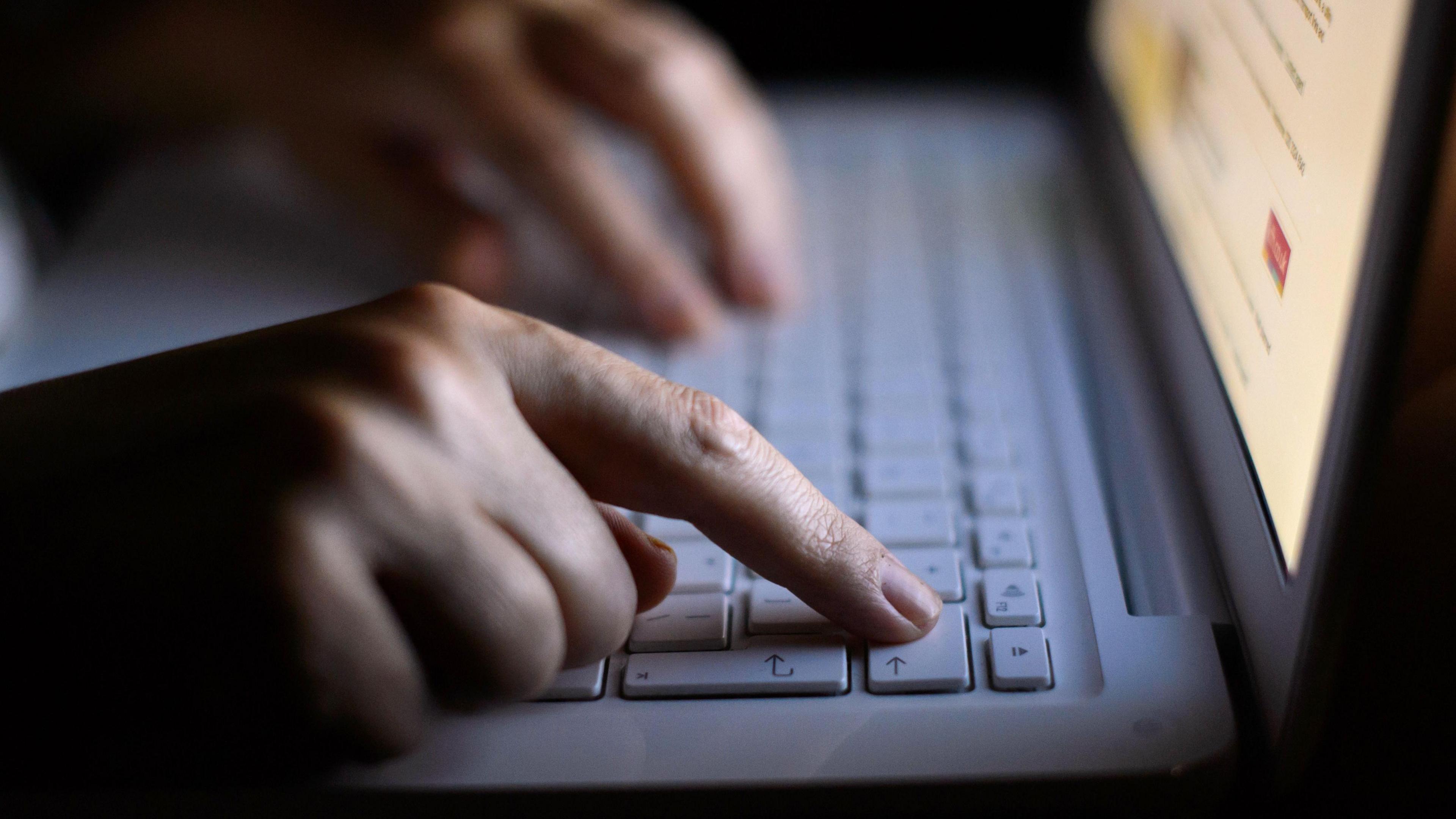 A person's hands type on a white laptop keyboard while looking at a website.