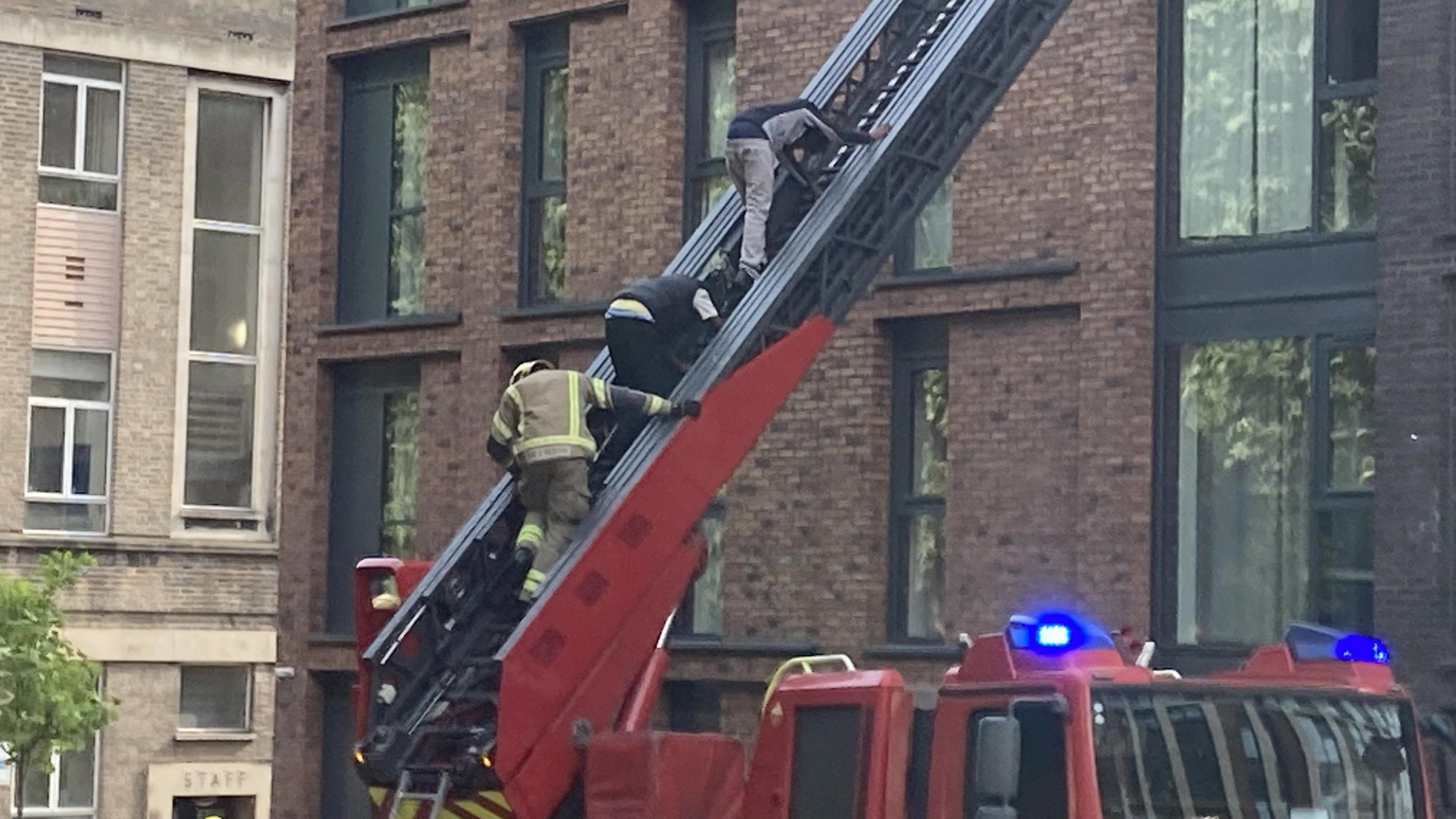 A firefighter helps two men down a ladder from a tower block in the centre of Bristol