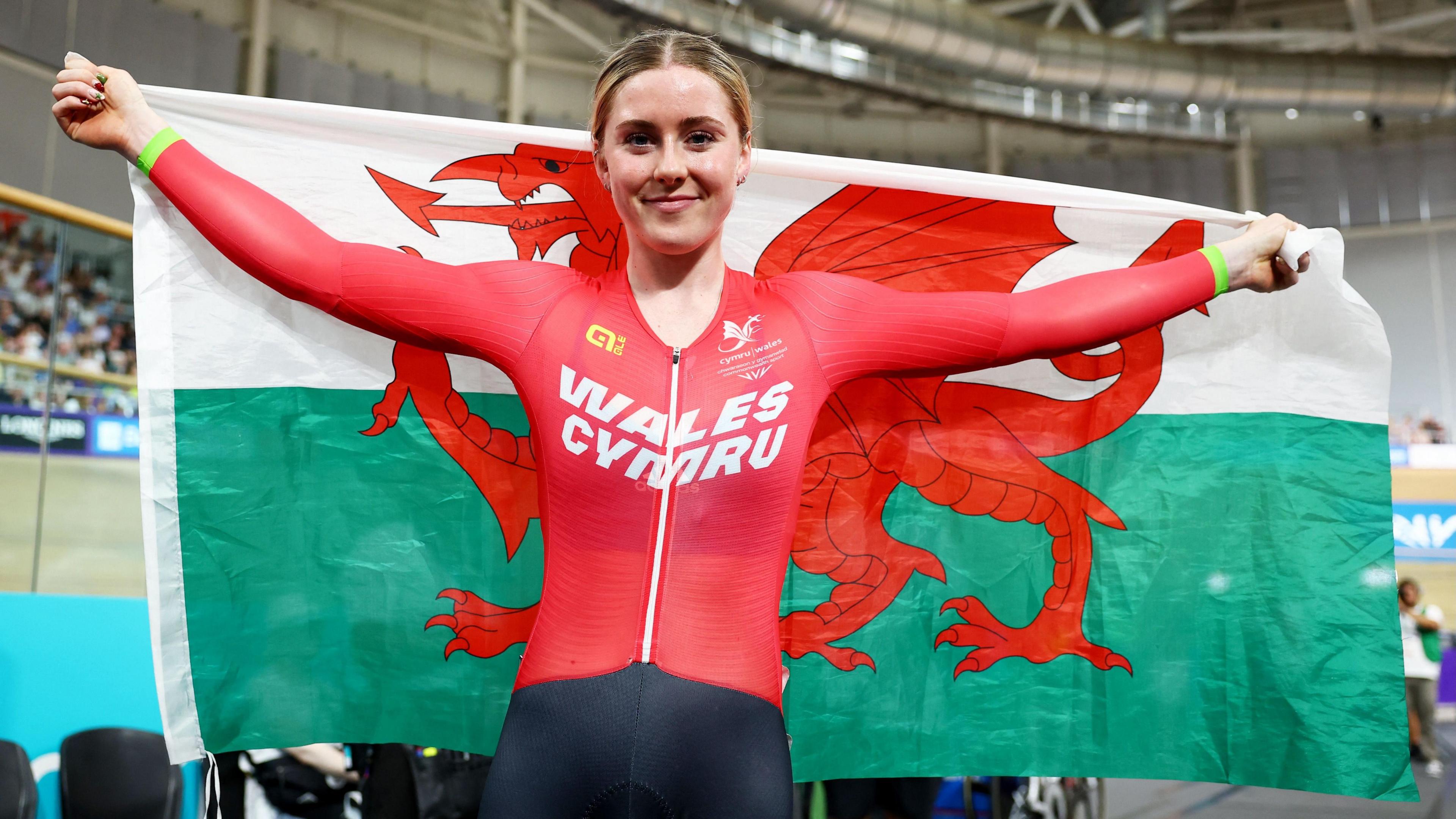 Emma Finucane wearing a red cycling vest holding up the Welsh flag