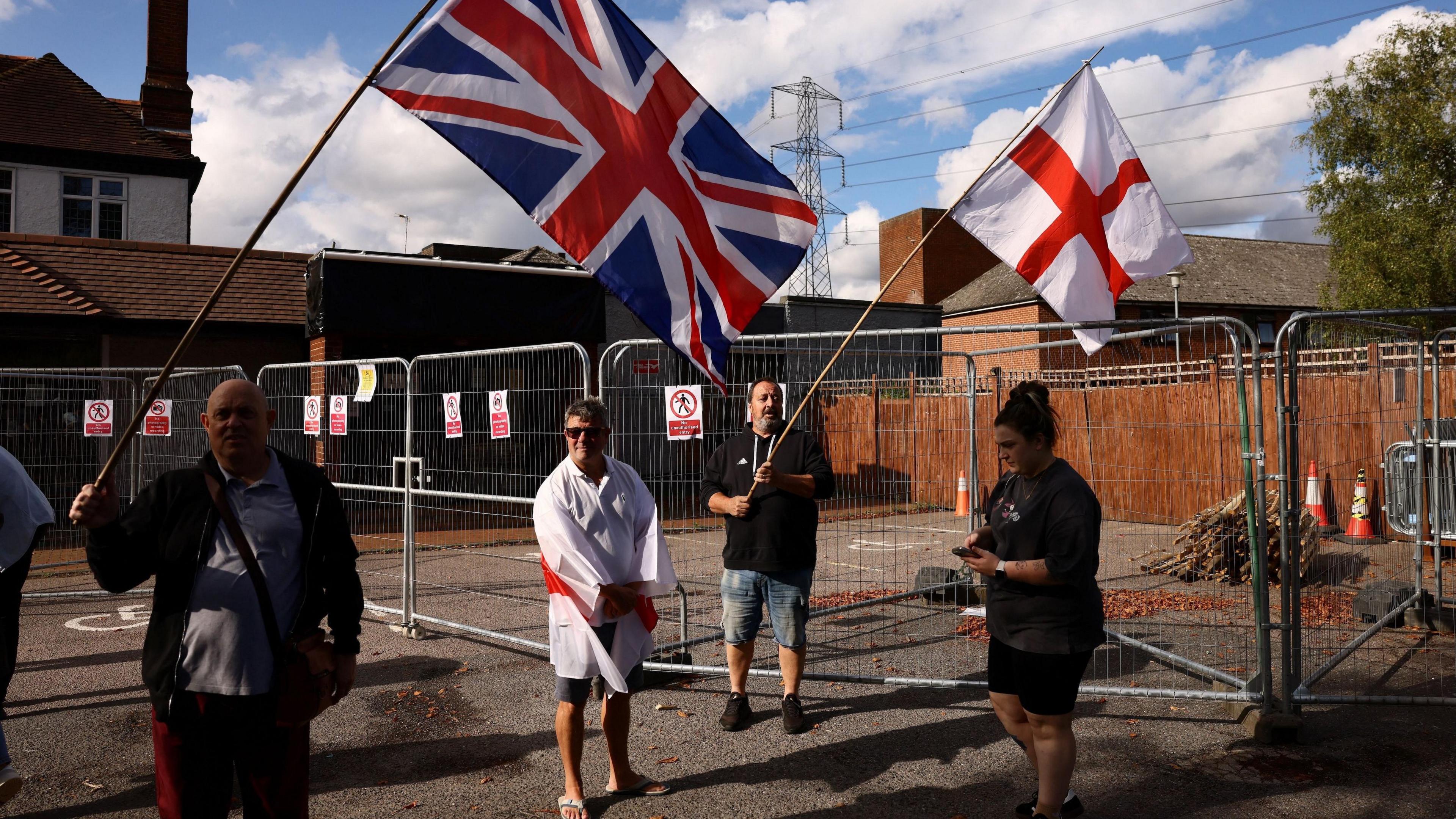 Protesters carry the Union Jack and St George's Cross flags above their heads on sticks outside the Bell Hotel in Epping.
