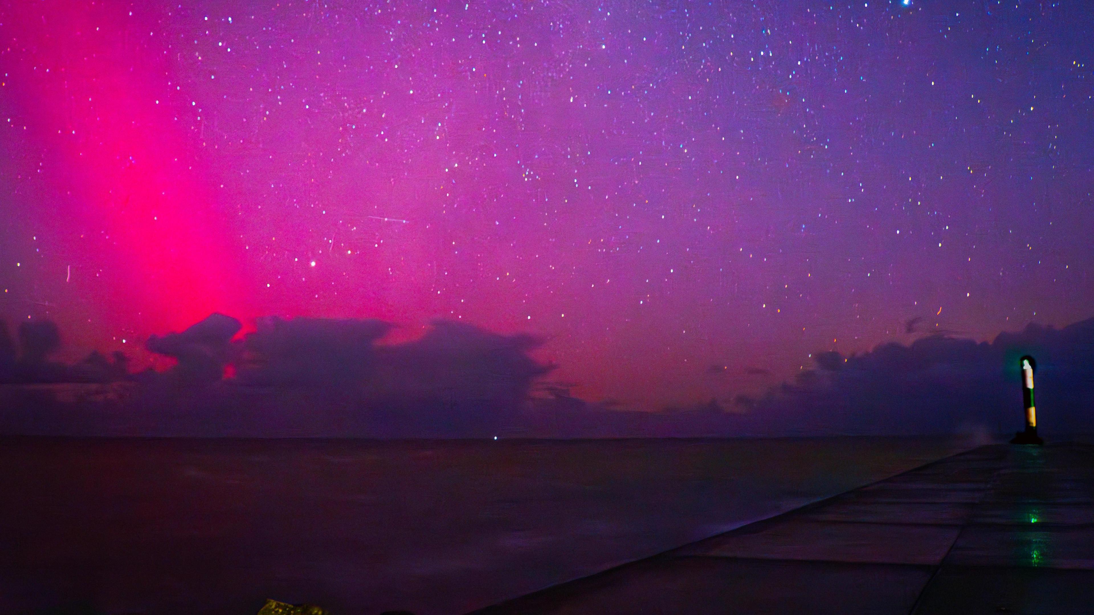 Pink and purple skies above the sea with dark clouds just above the water and a pier visible to the right