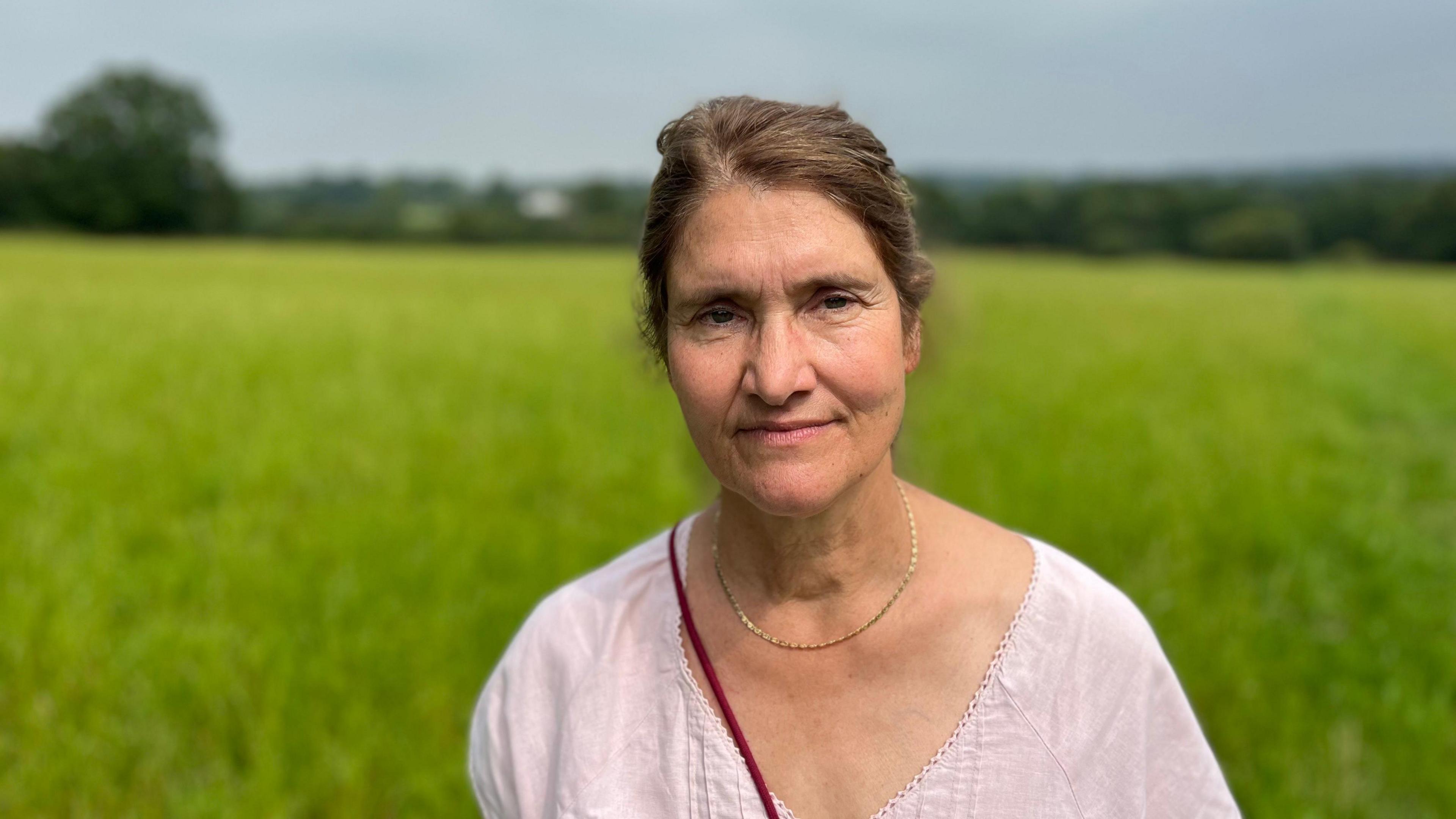 A woman looks straight into the camera with blurry grass behind her.