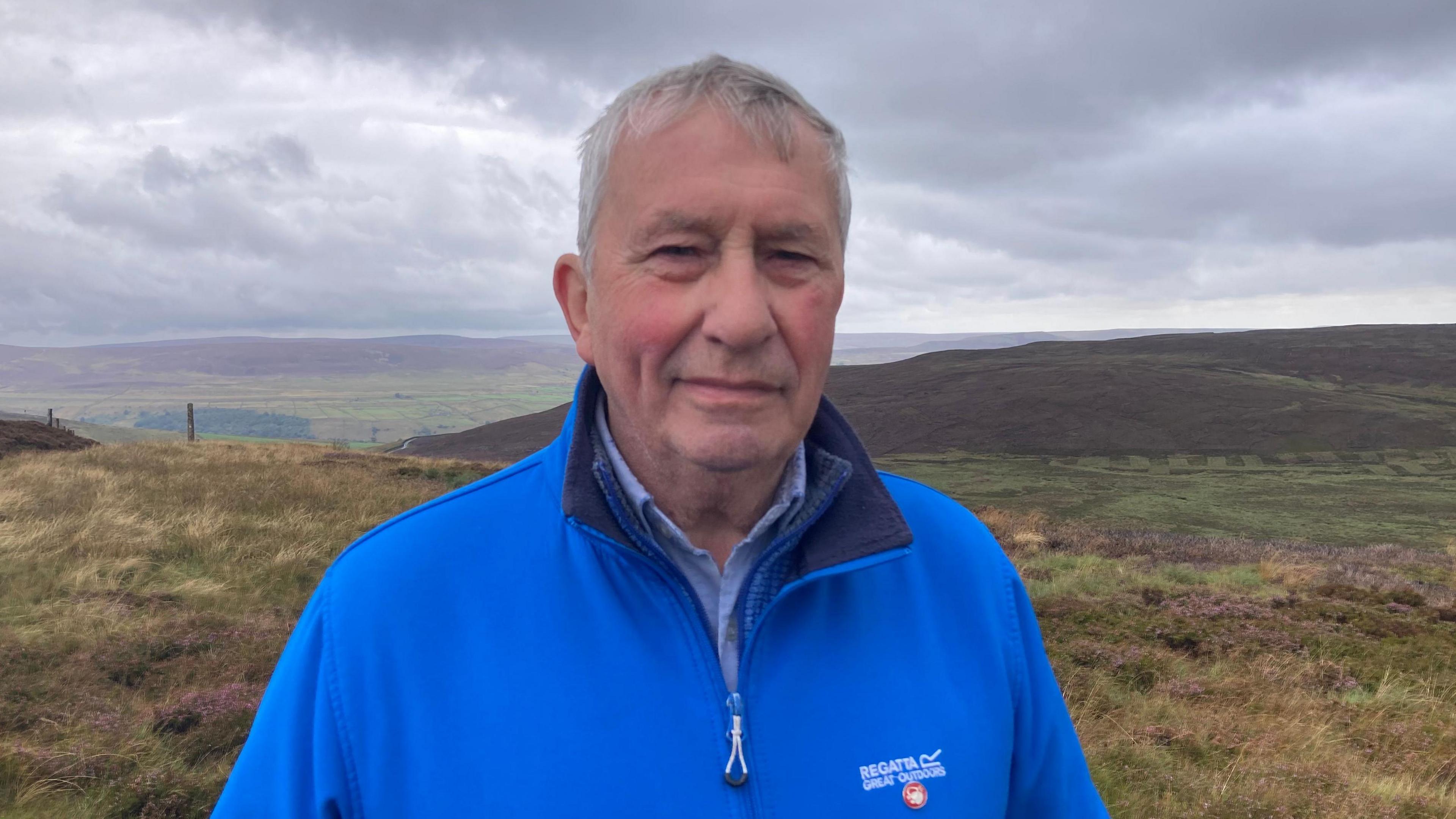 A picture of Earl Parker in front of the Yorkshire Dales National Park, smiling wearing a blue zip up fleece