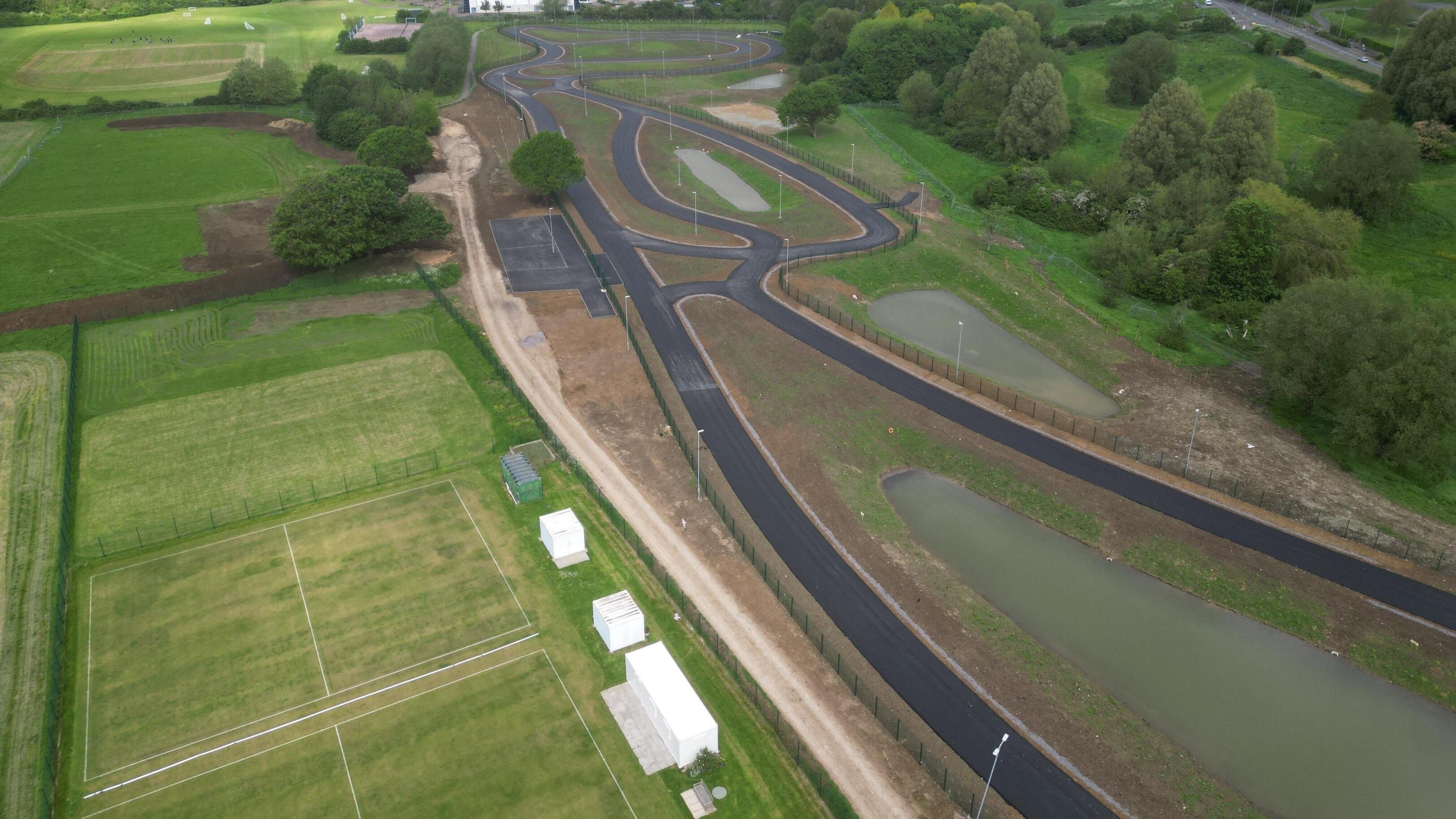 Overhead view of a tarmac cycling track with pitches next to it