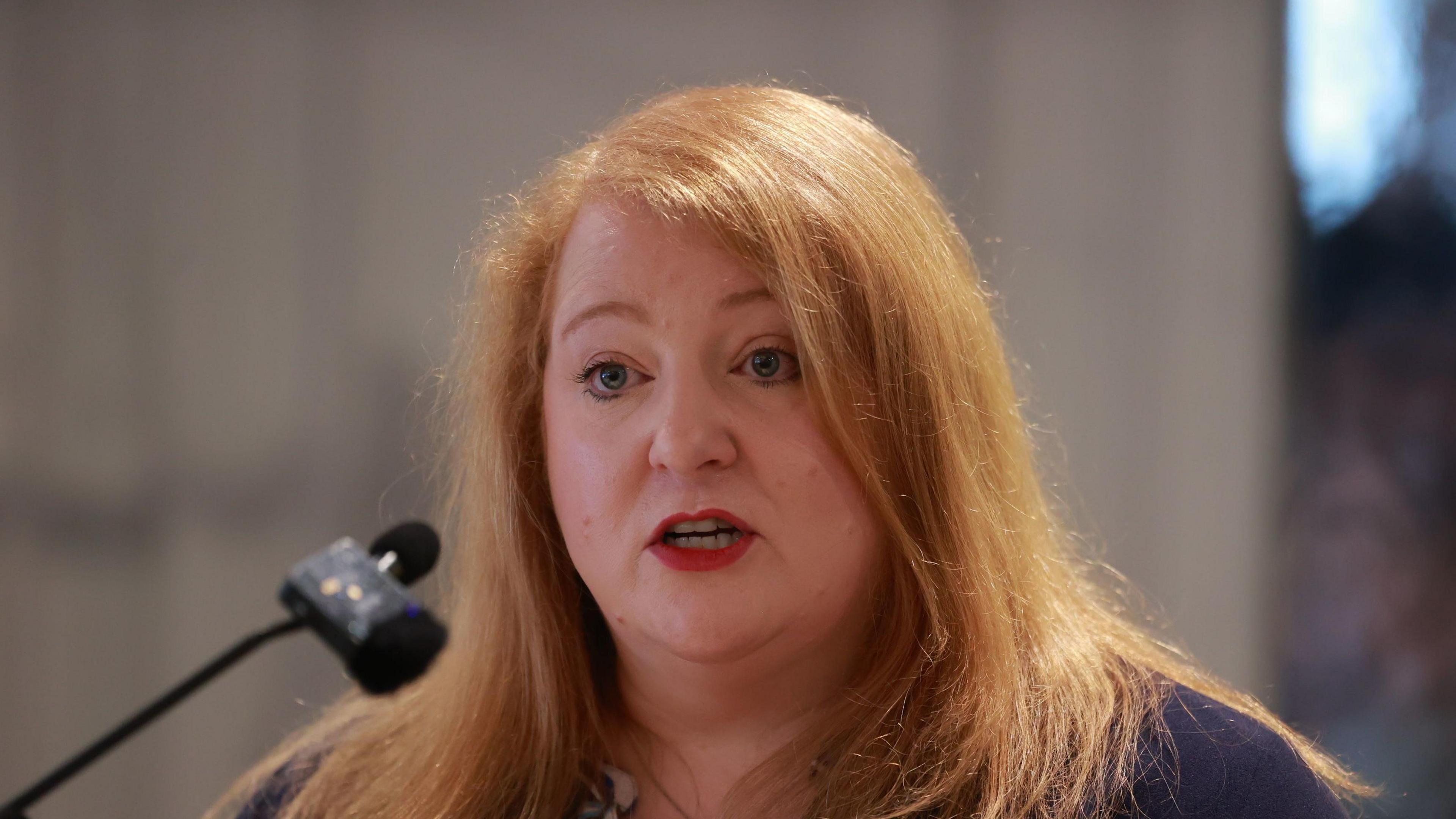 Naomi Long who has red hair, speaking into a microphone