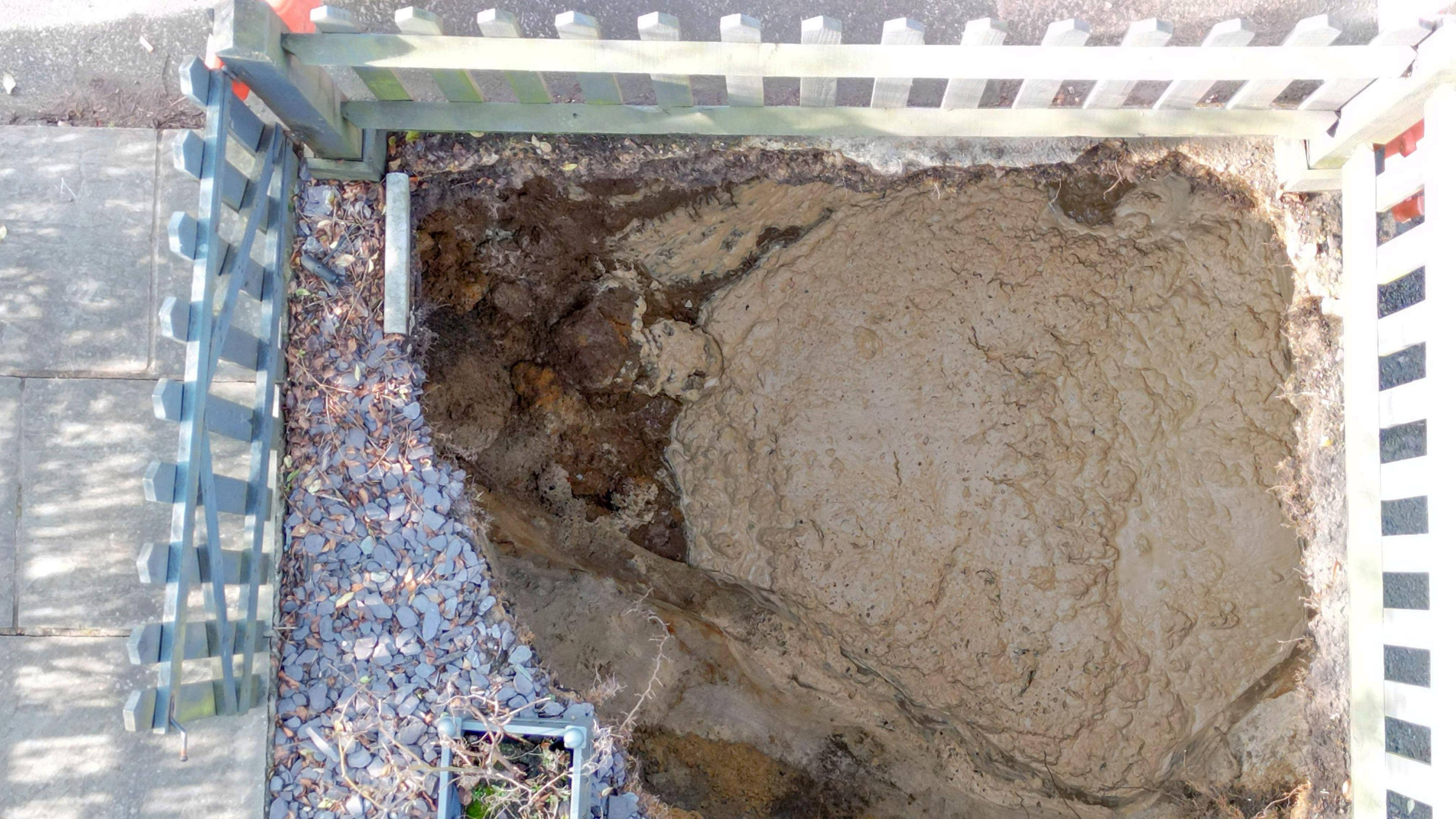 An aerial view of Rez Mira's garden disappearing into the sinkhole, surrounded by a white picket fence.