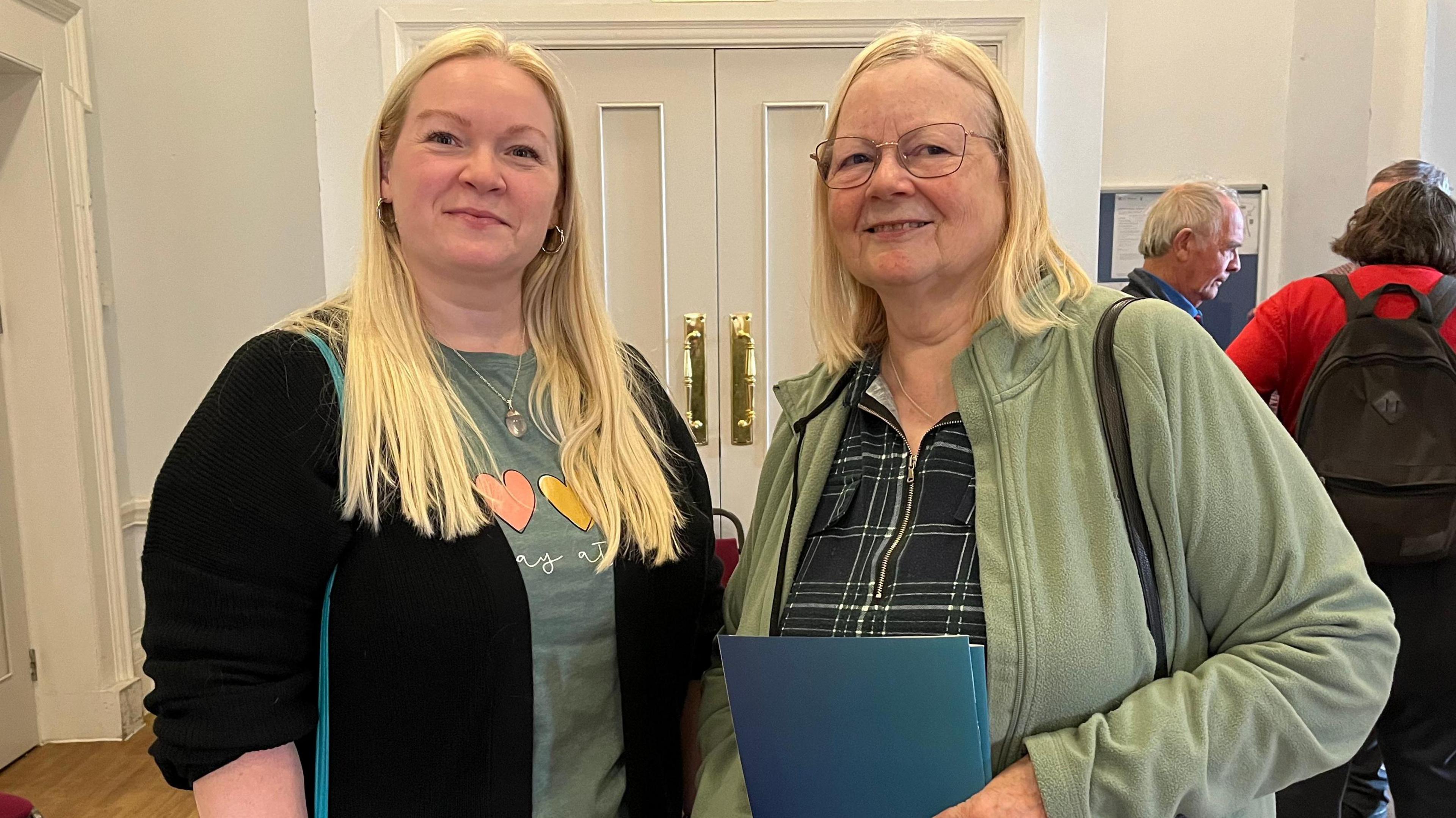 Kerry and Valarie Locke stand side by side. Both have pale blonde hair. Kerry wears a black cardigan and green t shirt. Valarie wears a green fleece and a dark green shirt. 