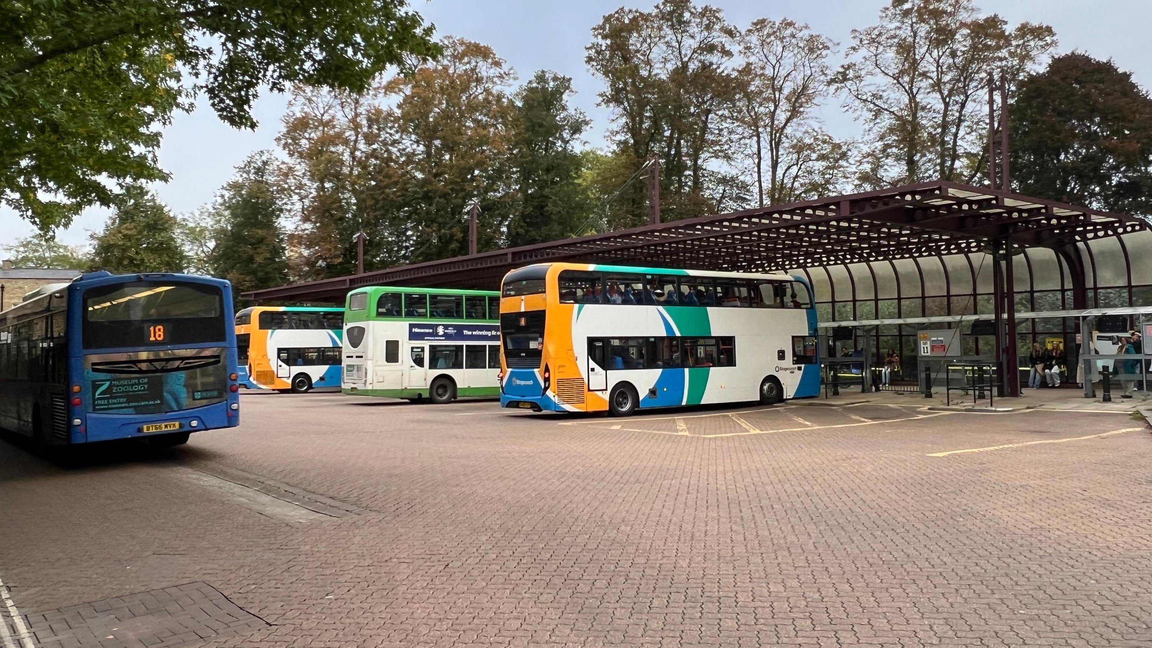 Four buses in a bus station. A covered pedestrian area is behind the vehicles. 