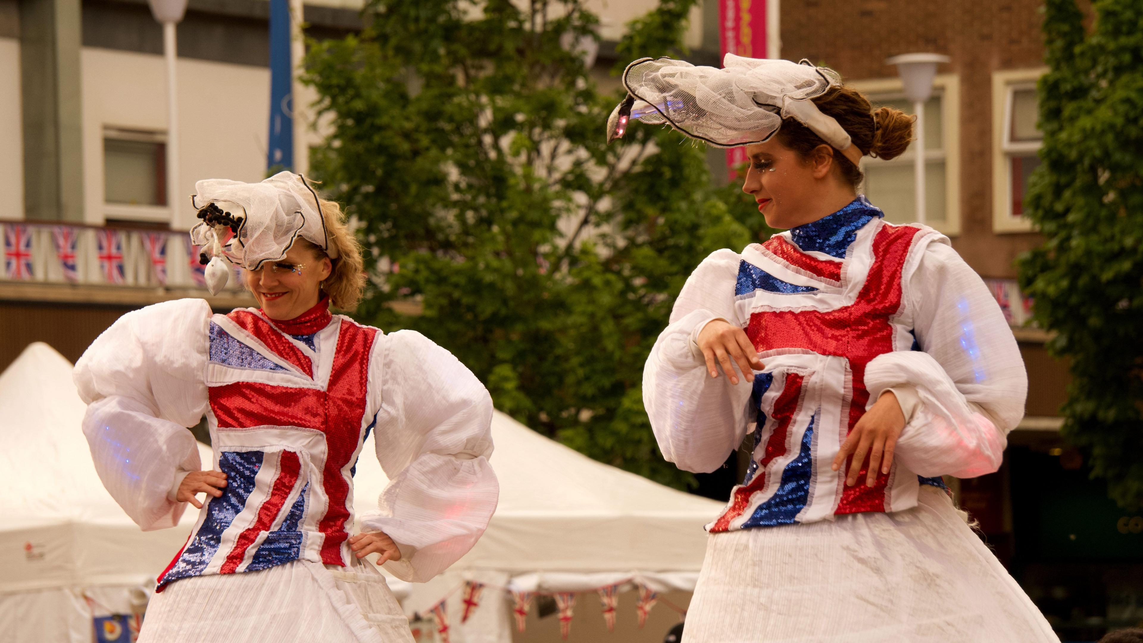 Two women on stilts with white dresses and red, white and blue sections on the front