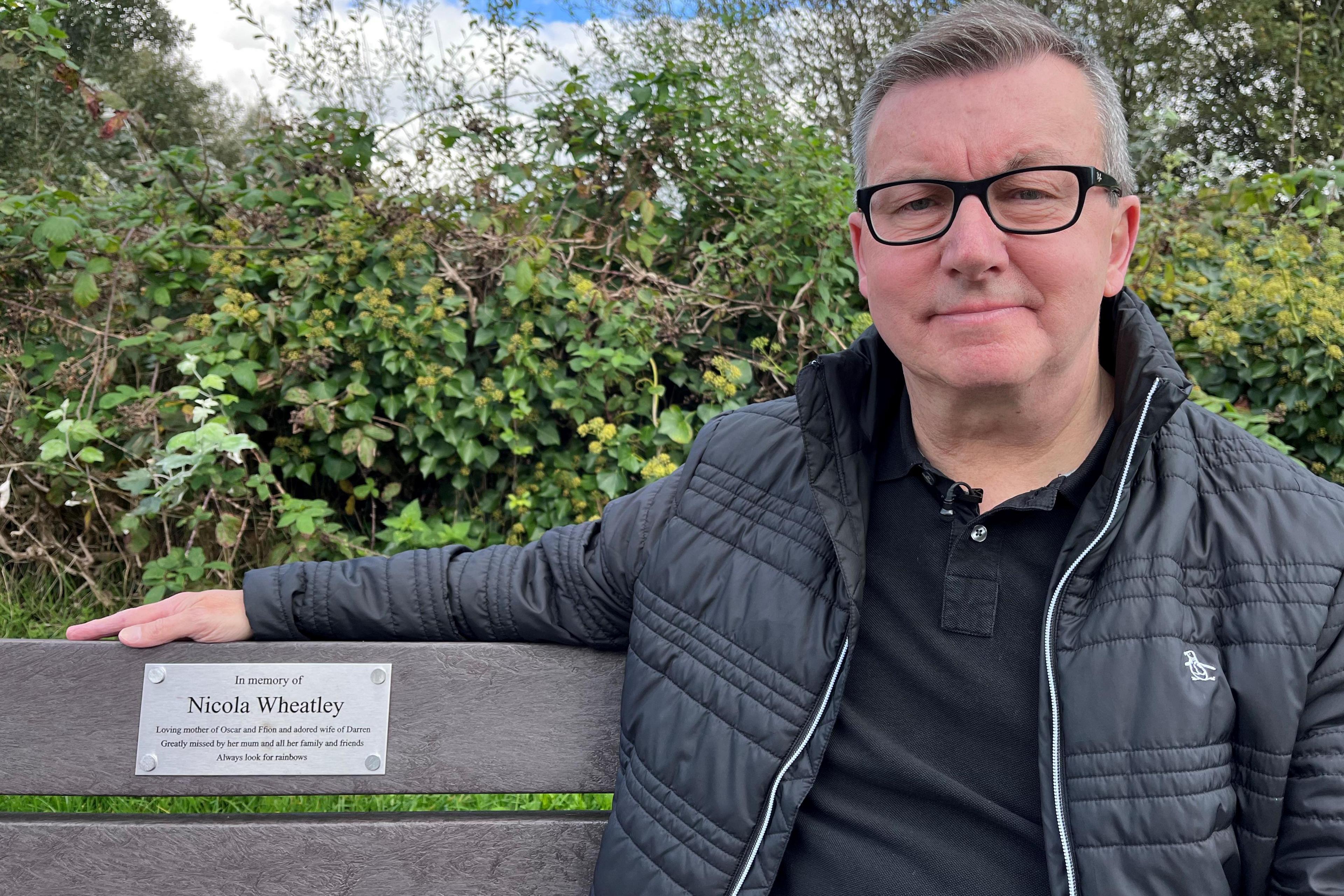 Darren on a bench he had dedicated to his wife. It reads: "Always look for rainbows".