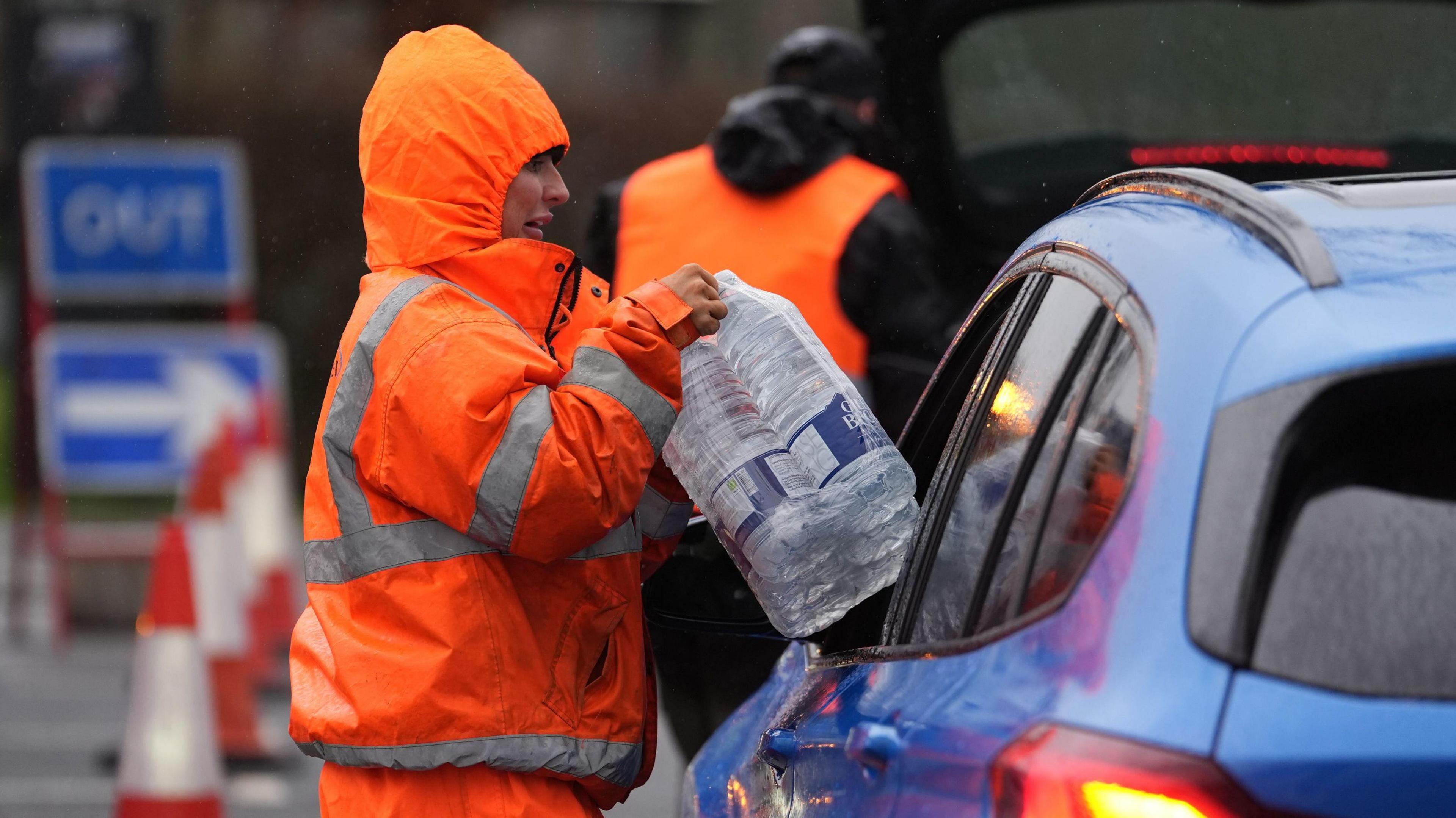 A worker hands someone in a car bottled water.
