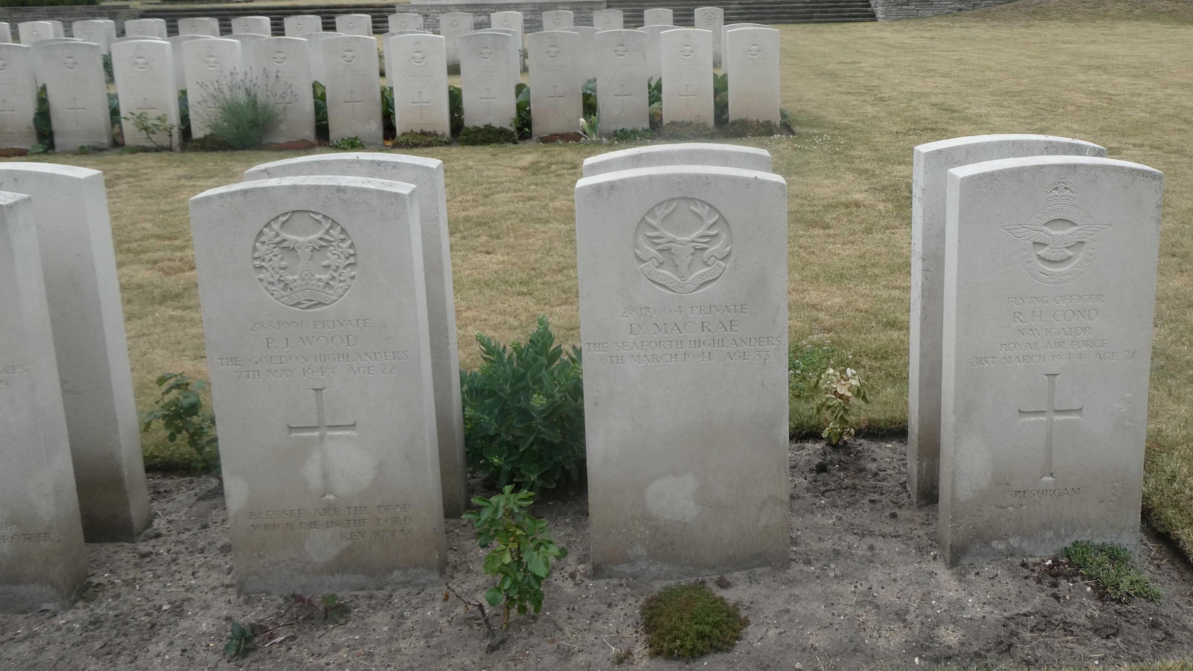 A neatly-spaced row of white headstones in the Commonwealth War Graves cemetery. They all contain an insignia at the top, a Christian cross and the name of the soldier who died.