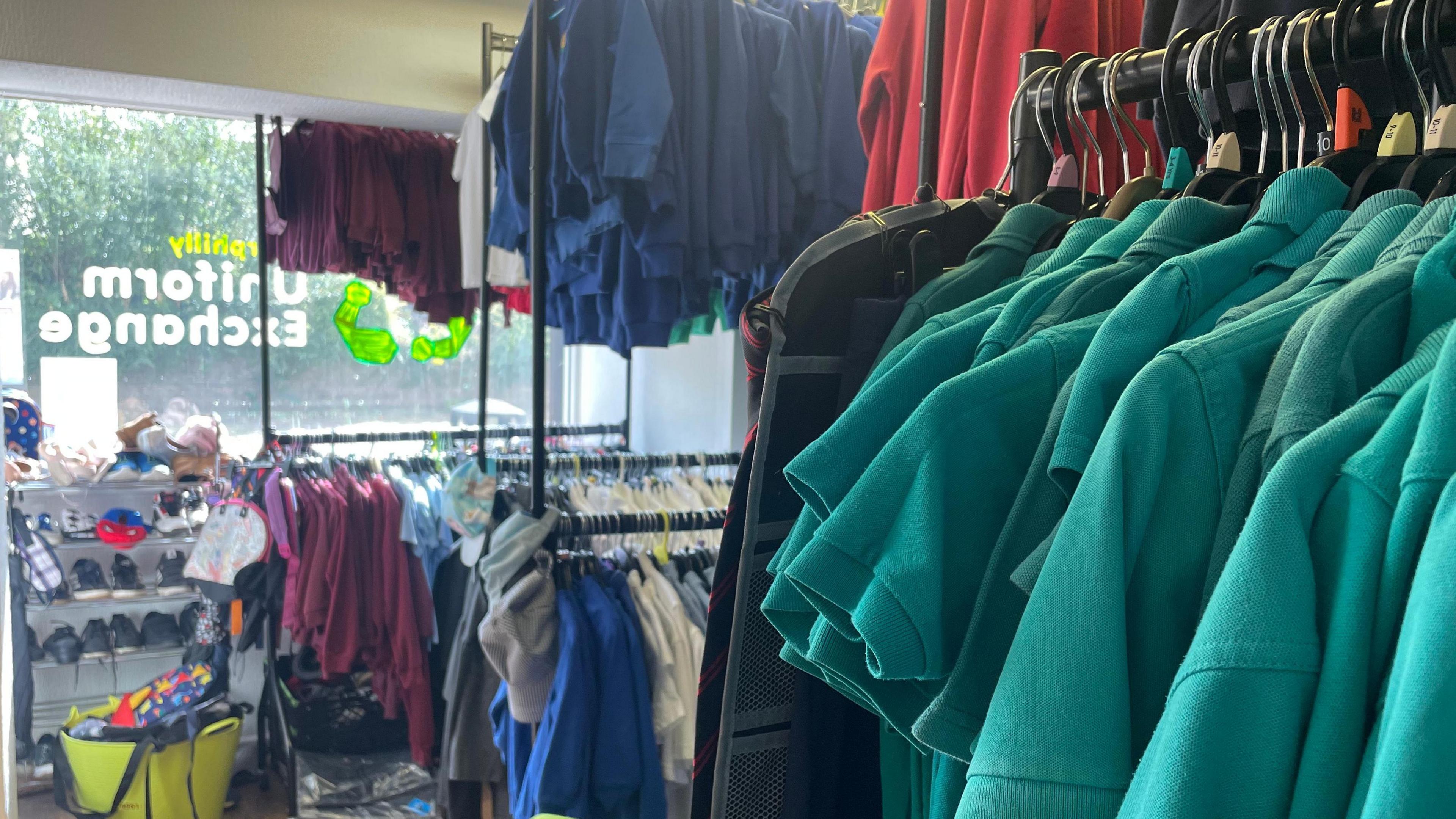 Racks of pre-loved school uniform and school shoes with green polo shirts in the foreground