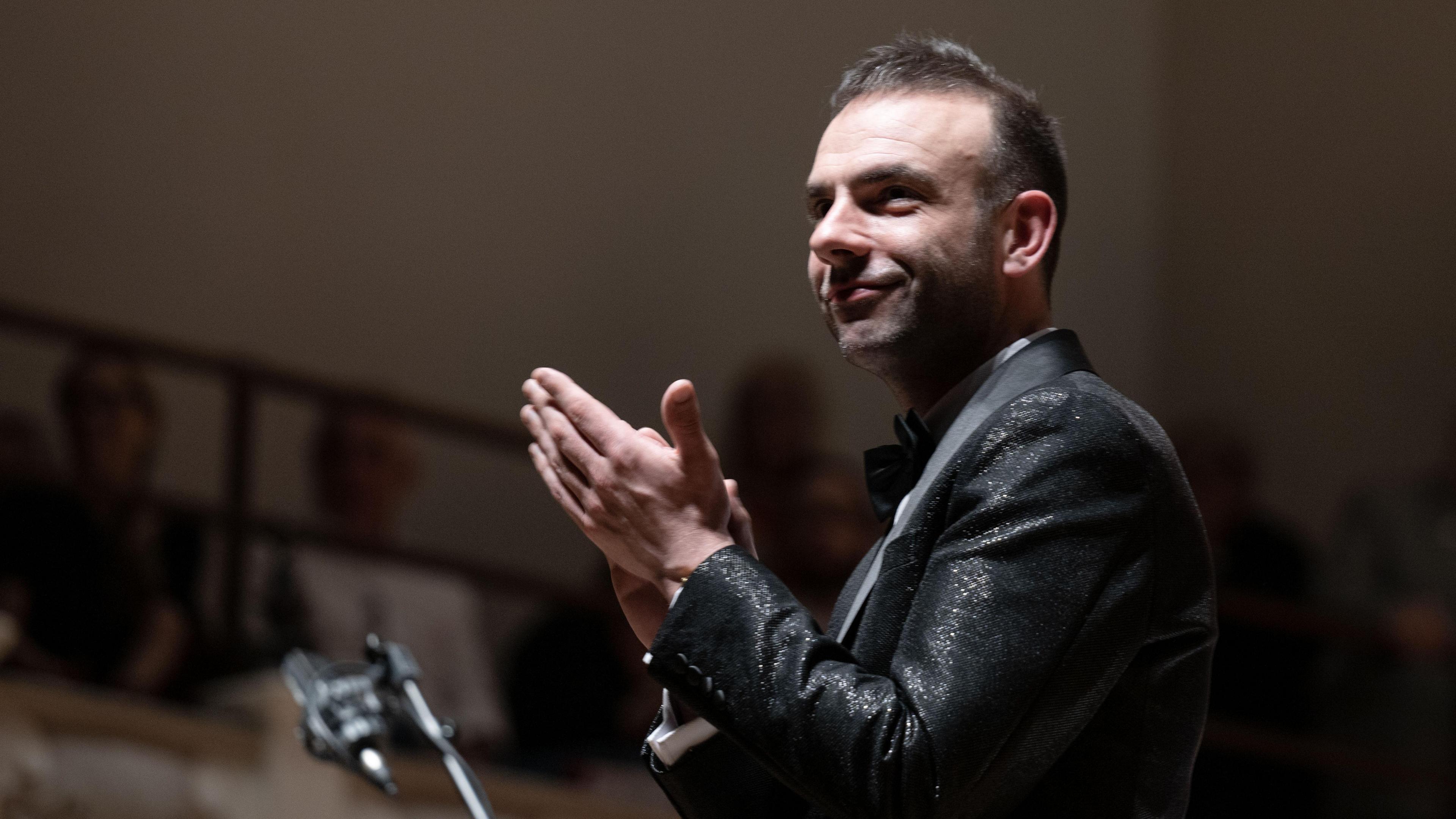 Matthew Jones at a music performance, wearing black tie and clapping and smiling