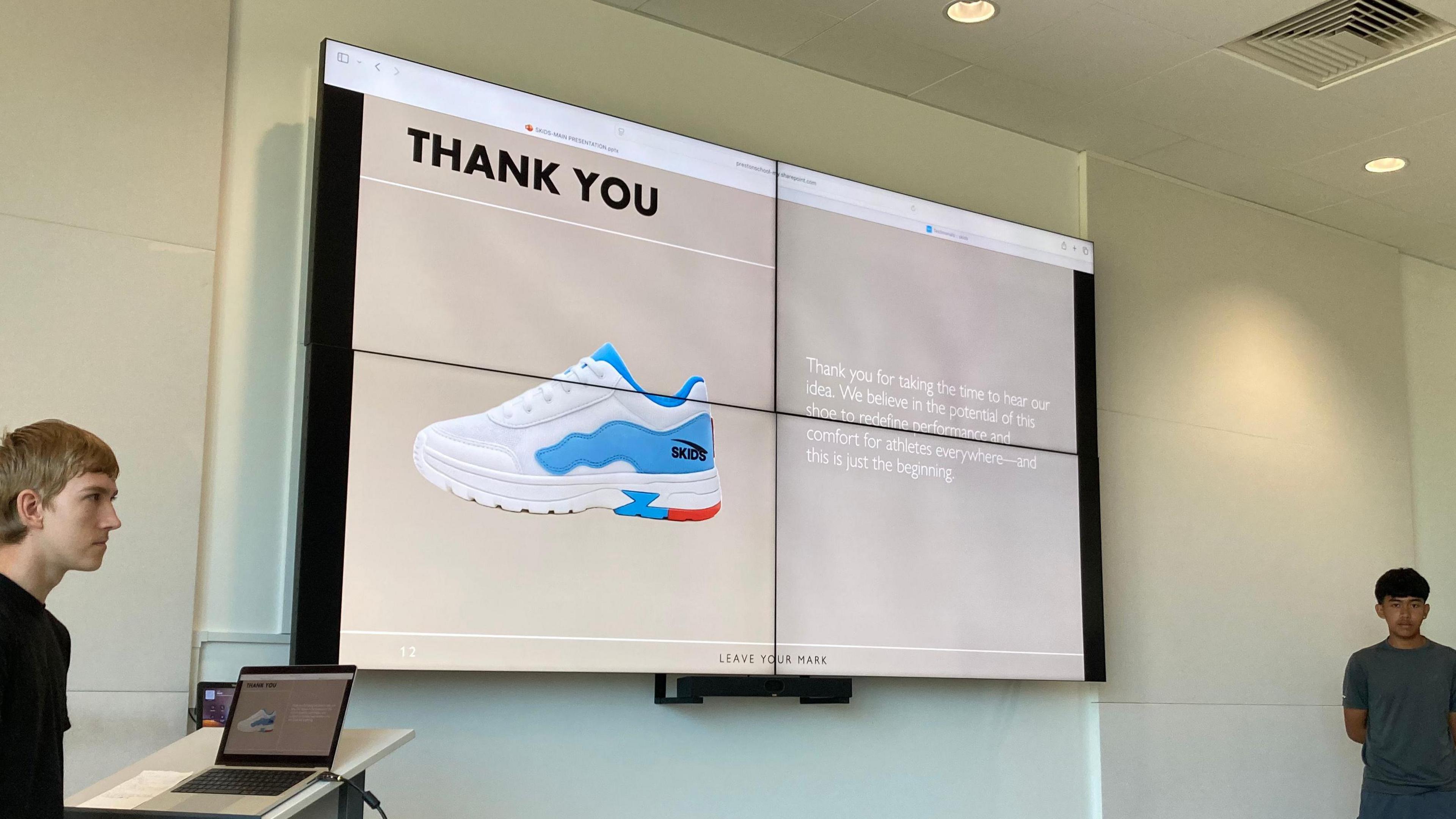 Two pupils stand either side of a white board that has an image of a training shoe projected onto it during a presentation at Clarks in Somerset