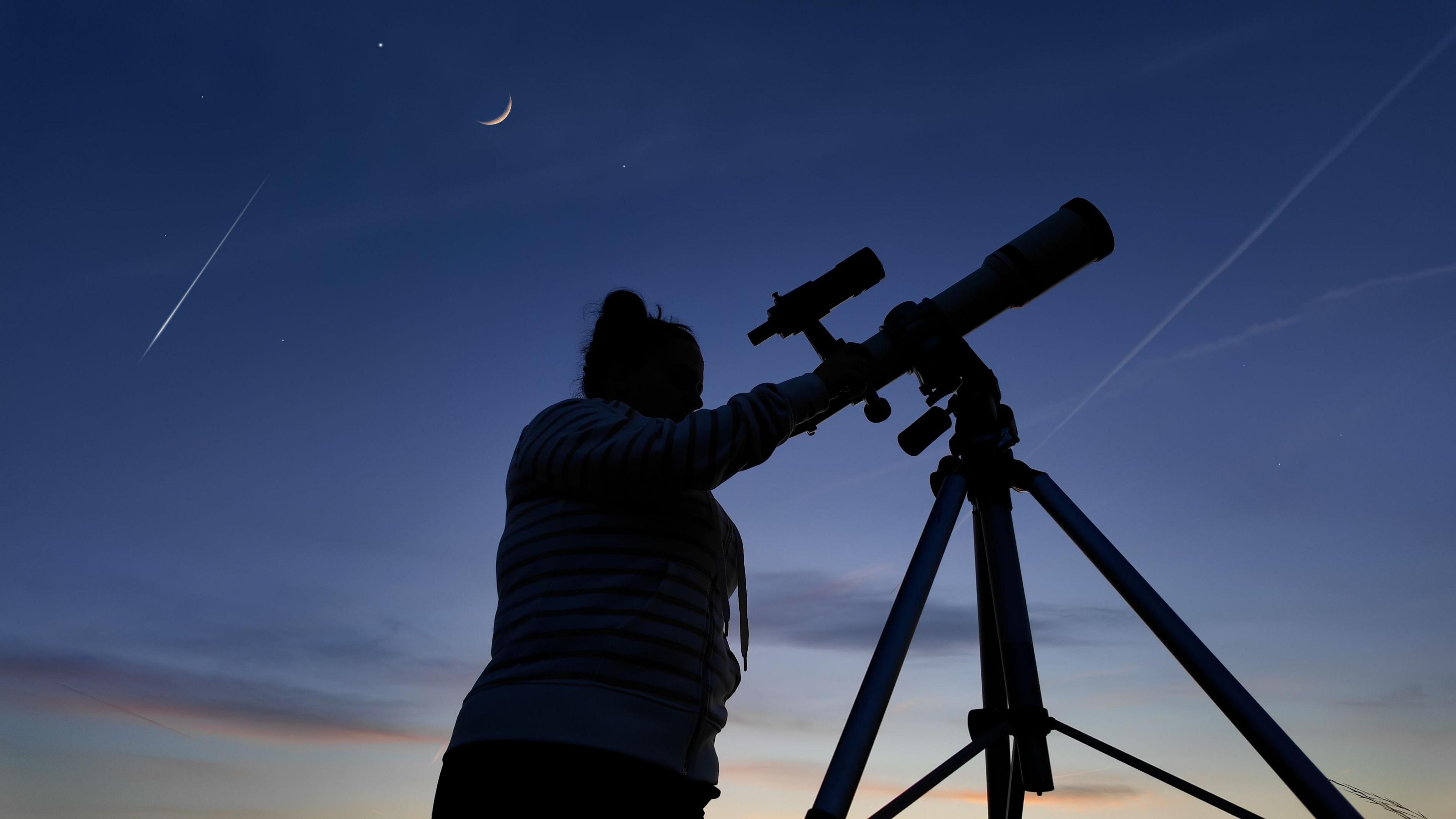 a woman looking at a meteor shower using a telescope