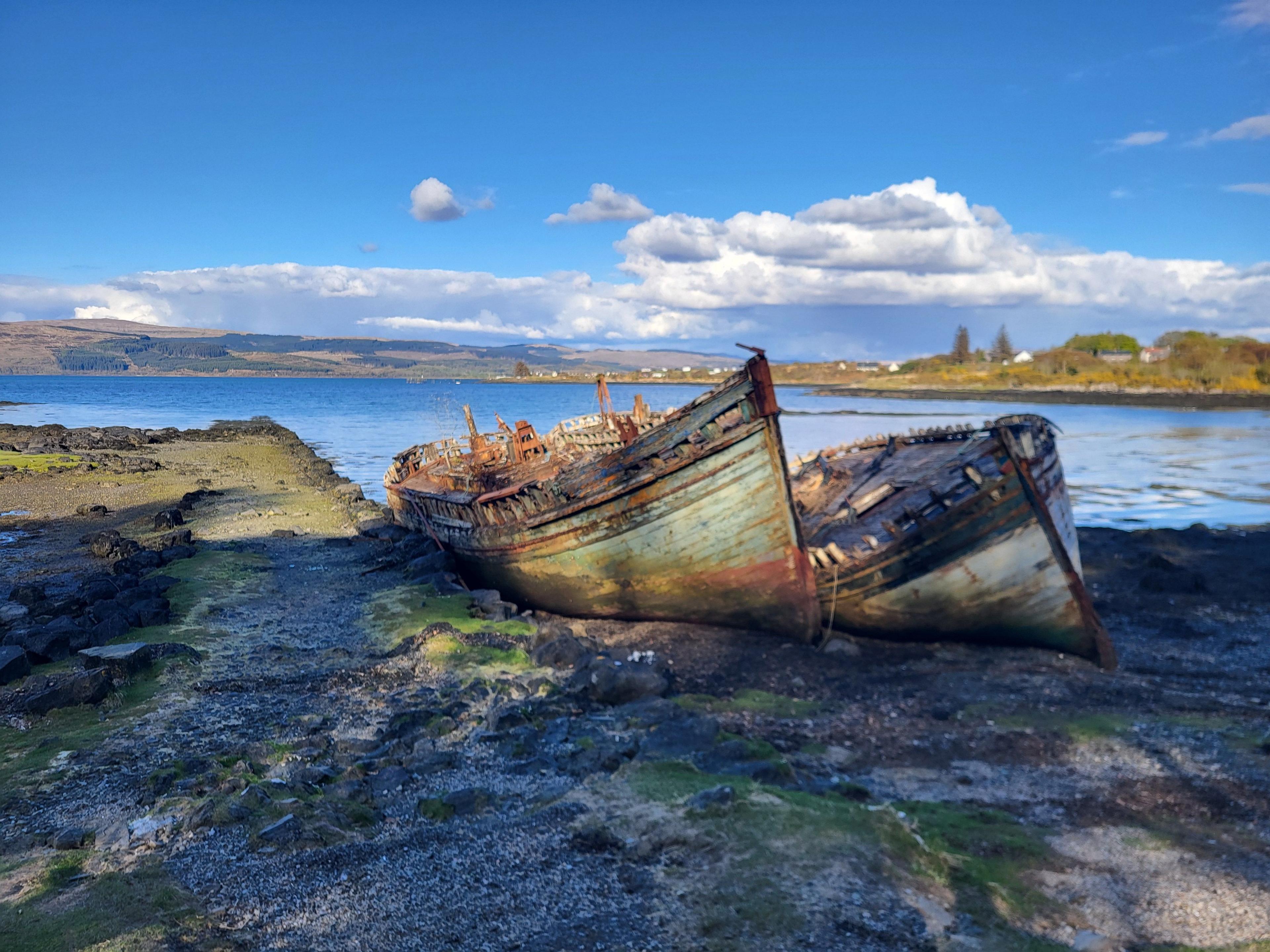 Two hulls of rusting boats near the shoreline