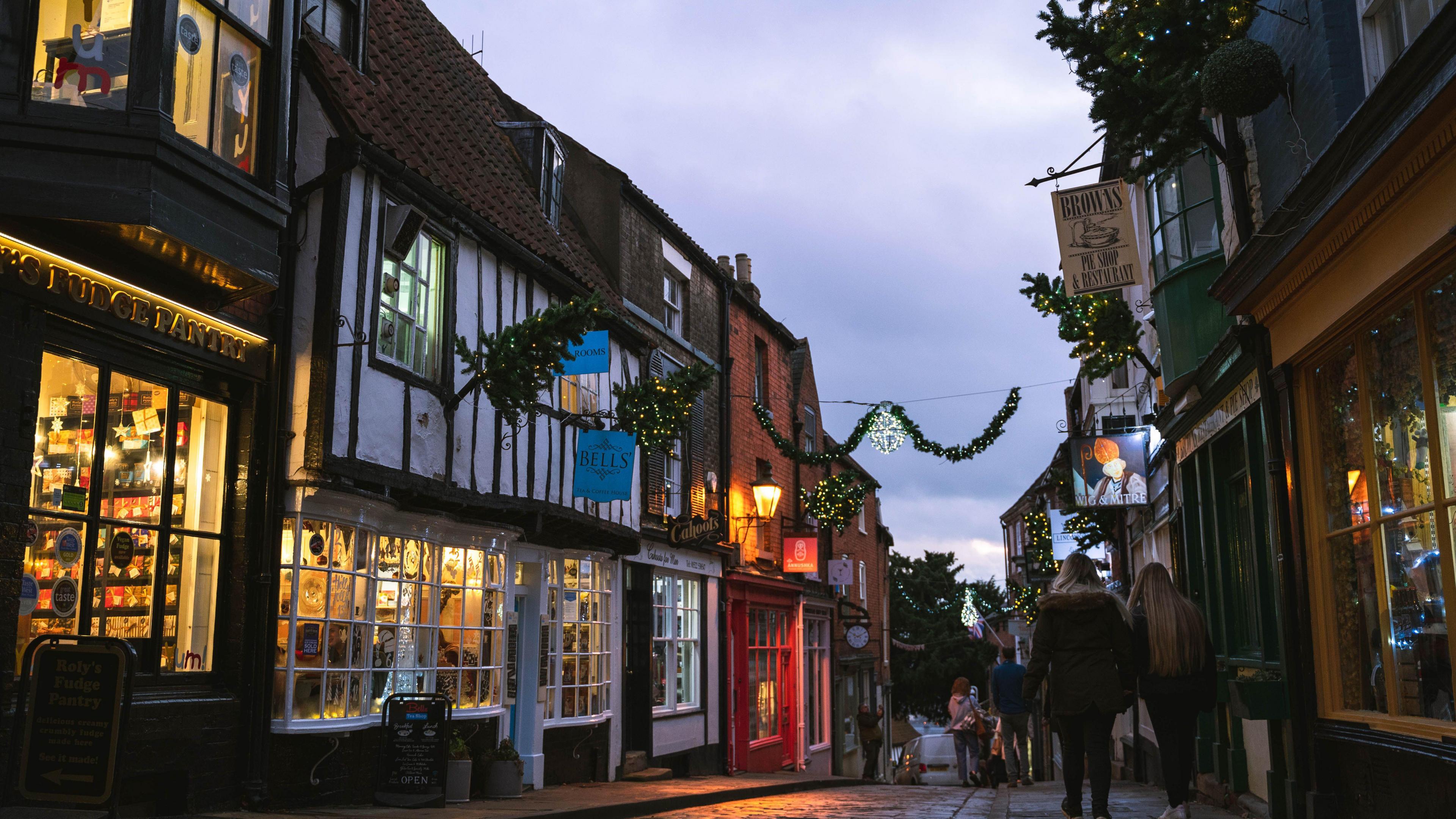 Lincoln's Bailgate shopping area, with Christmas lights hanging between shops. The street has cobbled flooring and vintage shop fronts.