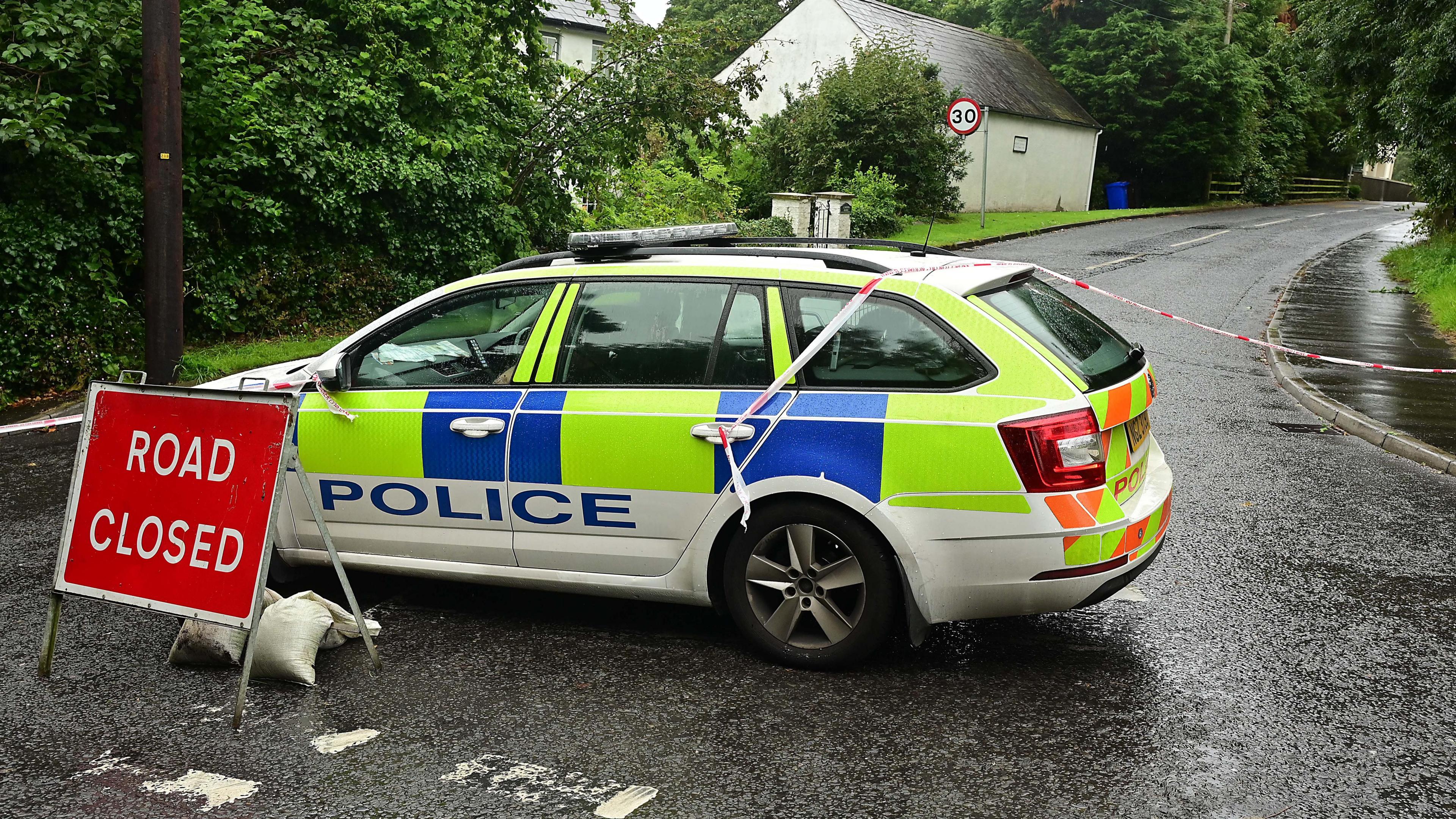 Road closed Church Road, police car parked with closure sign and police tape closing road off