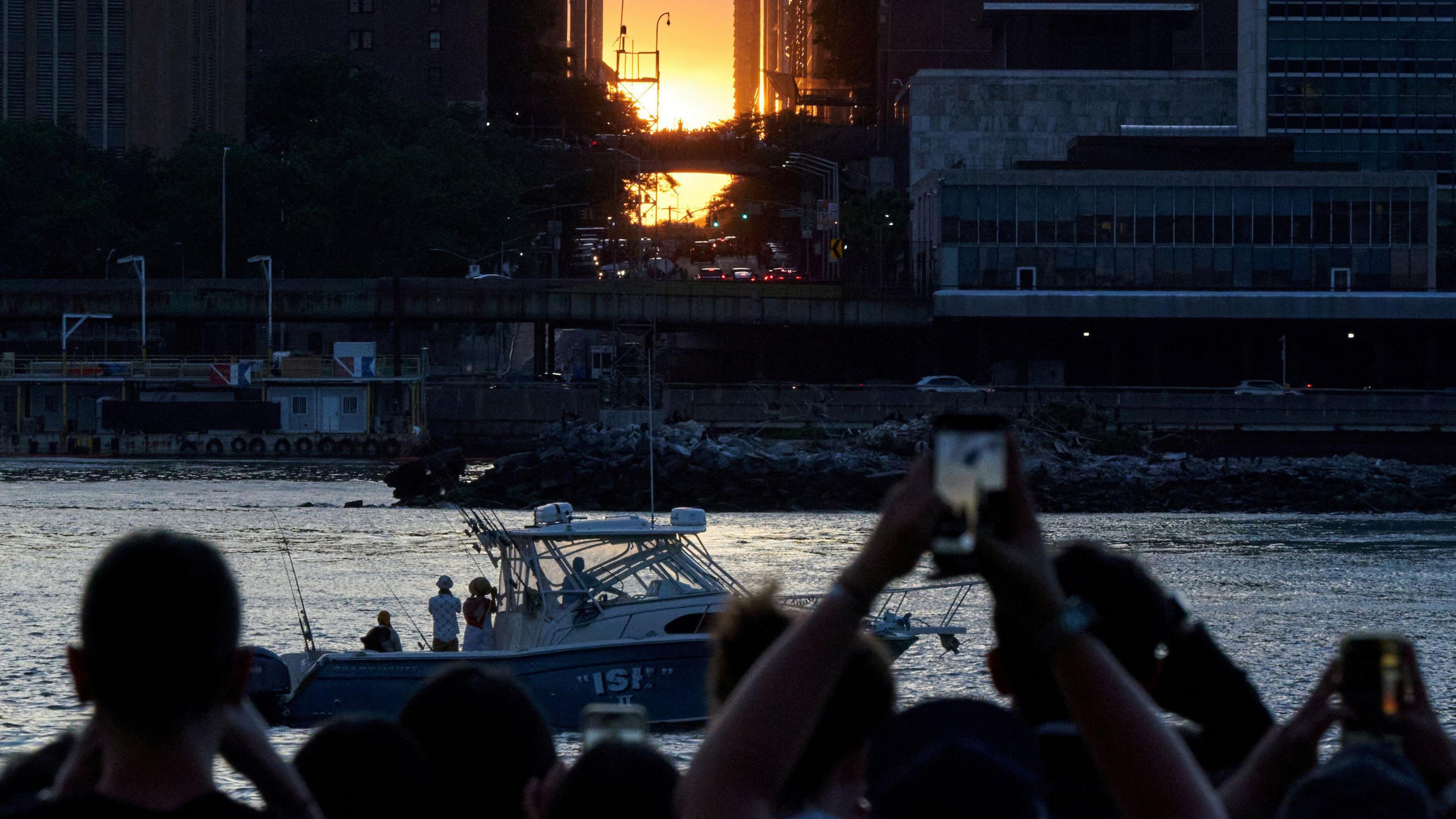 people photographing manhattanhenge sunset from across a river