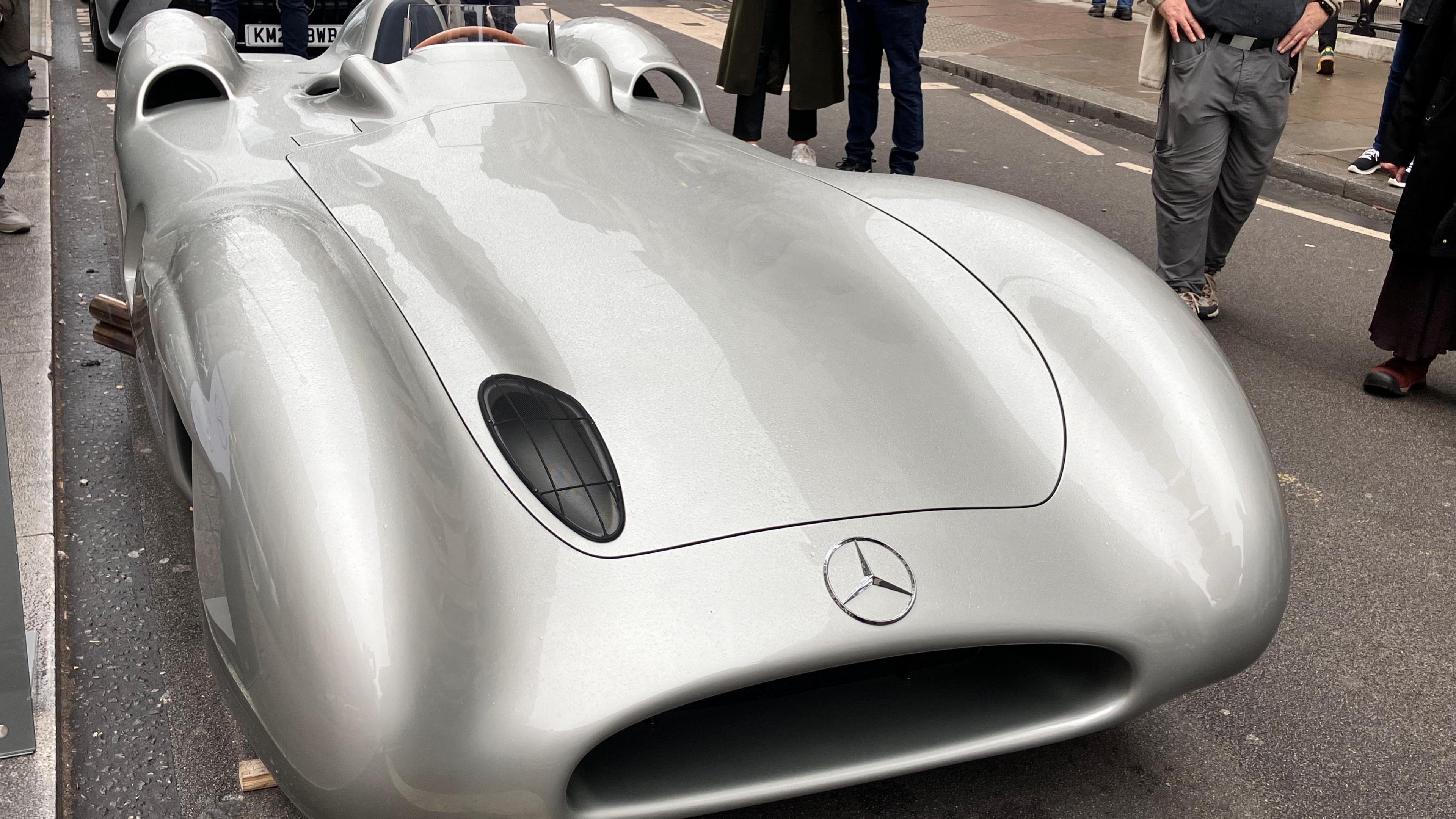 A silver Mercedes W196, a curved, futuristic-looking race car, parked on Pall Mall