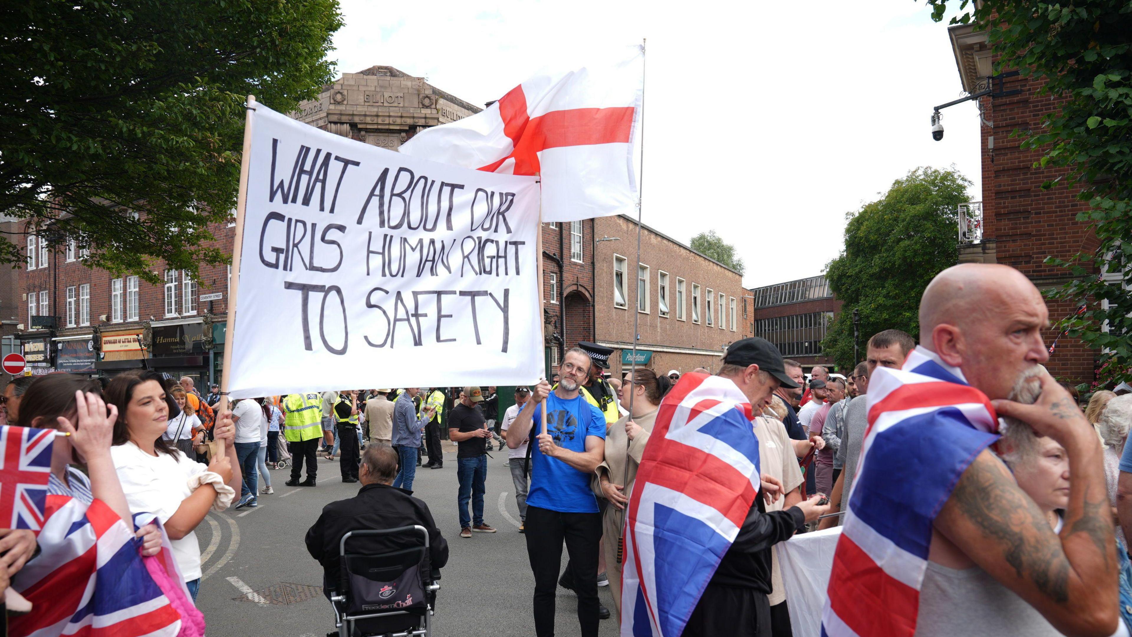 Two protesters holding a white banner stating 'What about our girl's human right to safety