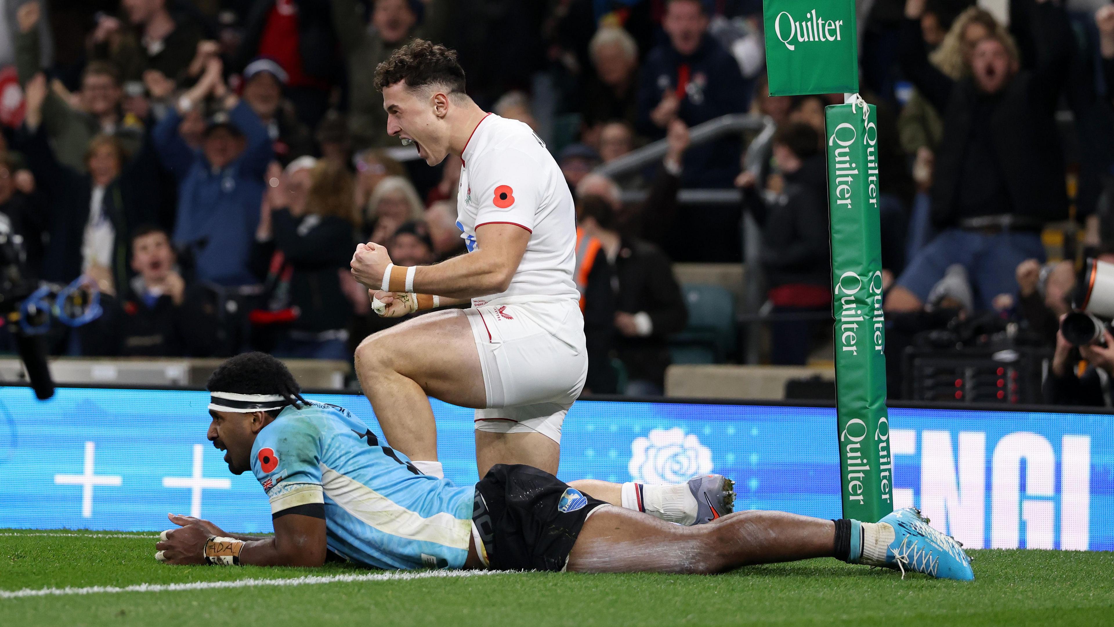 Henry Arundell kneels on the floor and clenches his fists in celebration after scoring a try for England, while Fiji's 