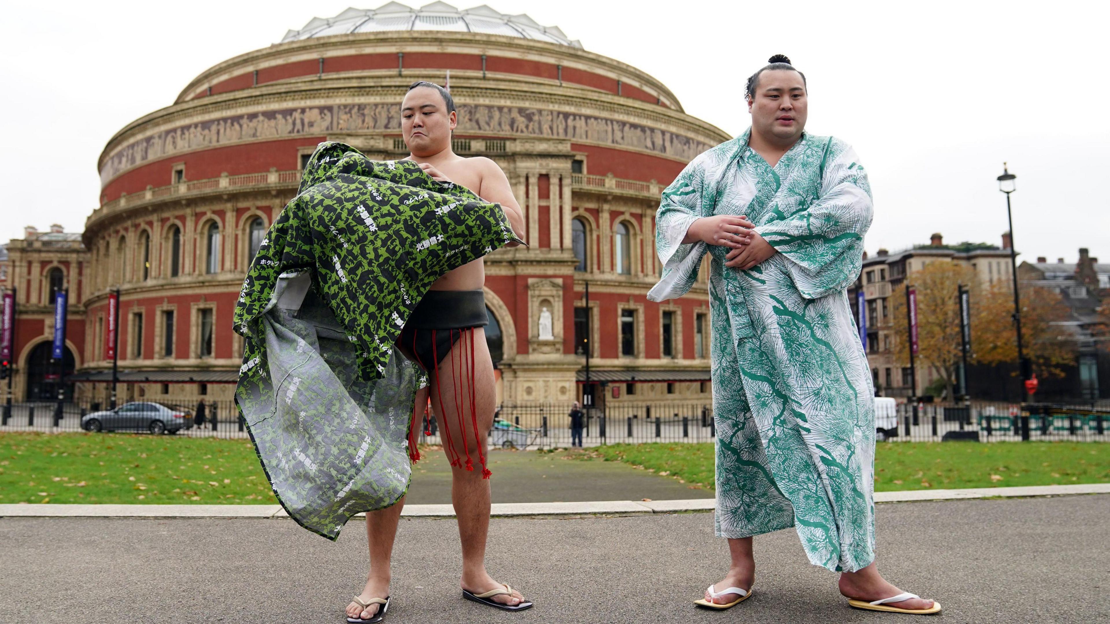 Sumo wrestlers Kitanowaka Daisuke (right) wears a green and white patterned yukata and Fukutsuumi Akira (left) is taking off a green yukata. The Royal Albert Hall can be seen in the background.