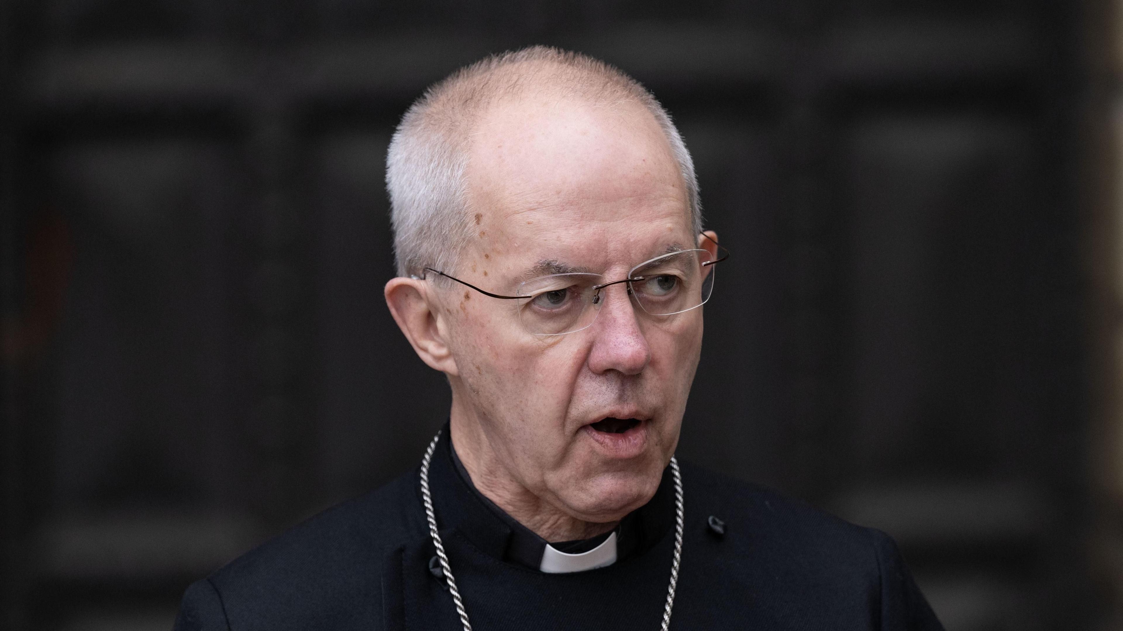 Justin Welby, the Archbishop of Canterbury, pictured wearing his cassock while standing in front of some large and dark wooden doors.